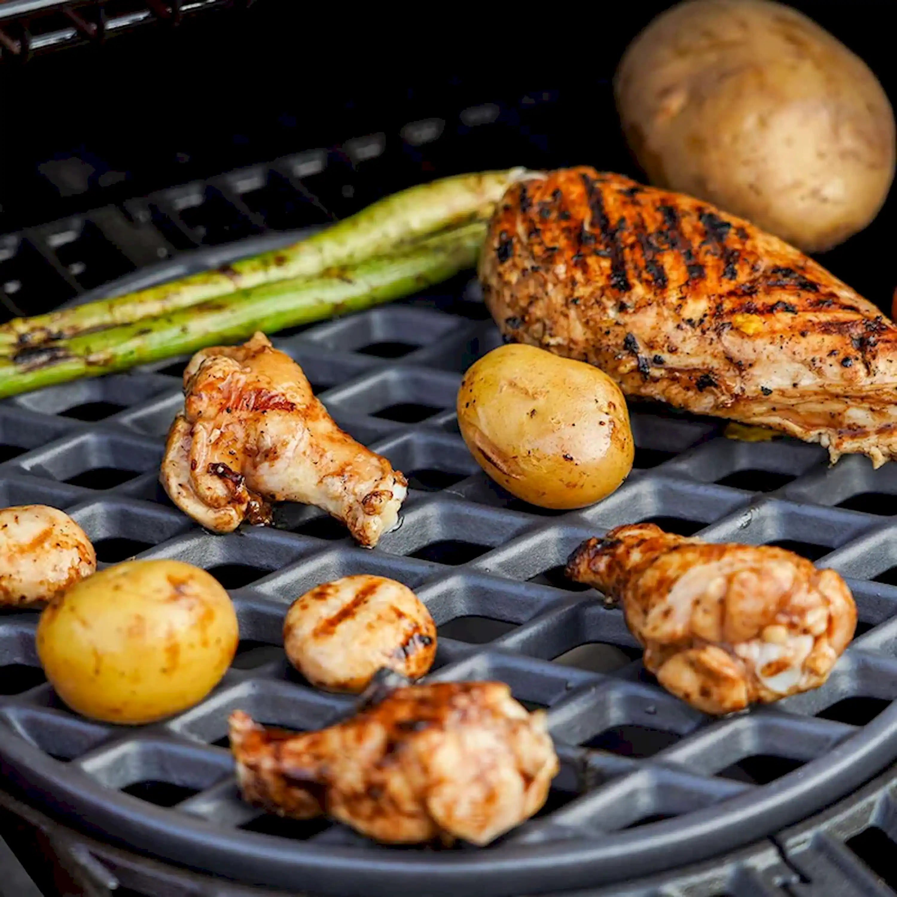 Round cast iron grill grate with seared chicken and sliced vegetables
