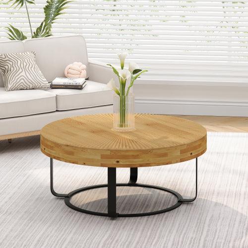 Round wooden coffee table with radial carved top, black metal base, and glass vase.