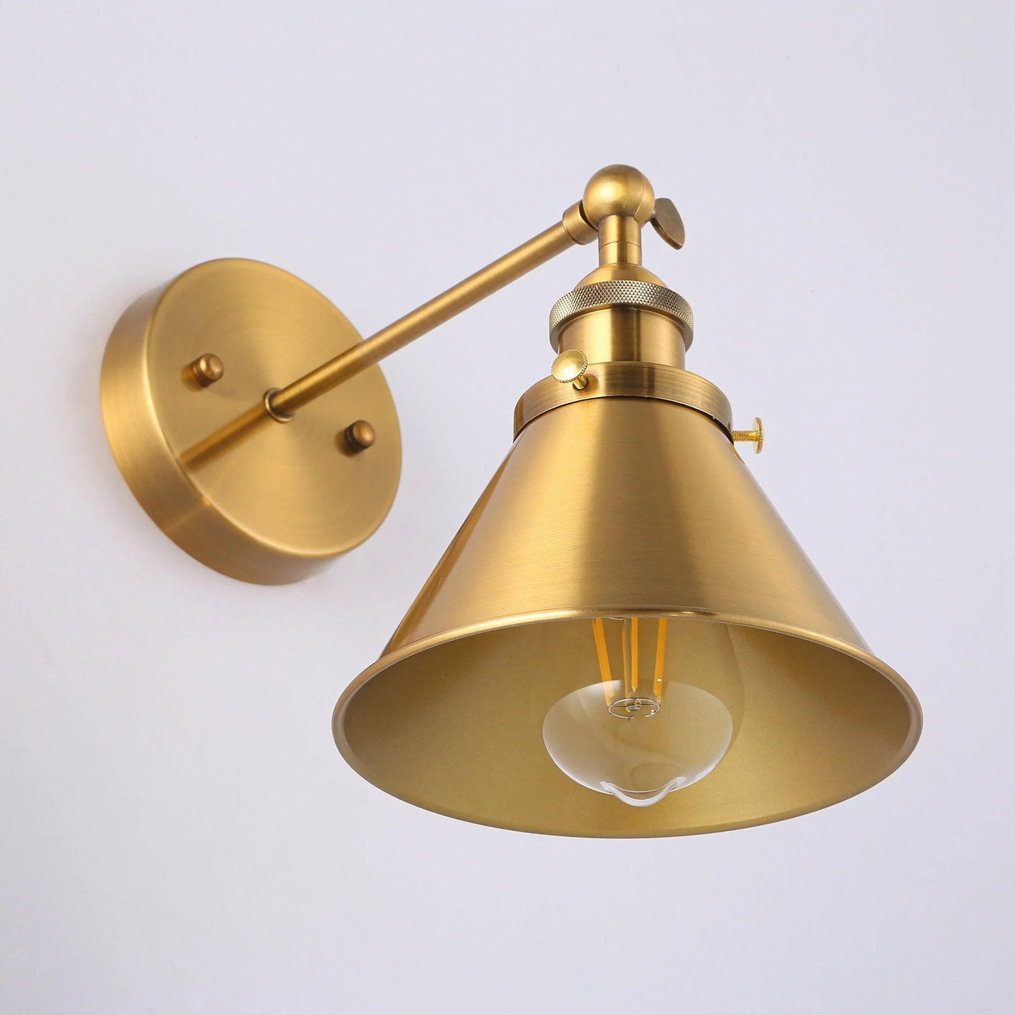 Golden brass wall sconce close-up with round backplate, bell shade, and glowing bulb