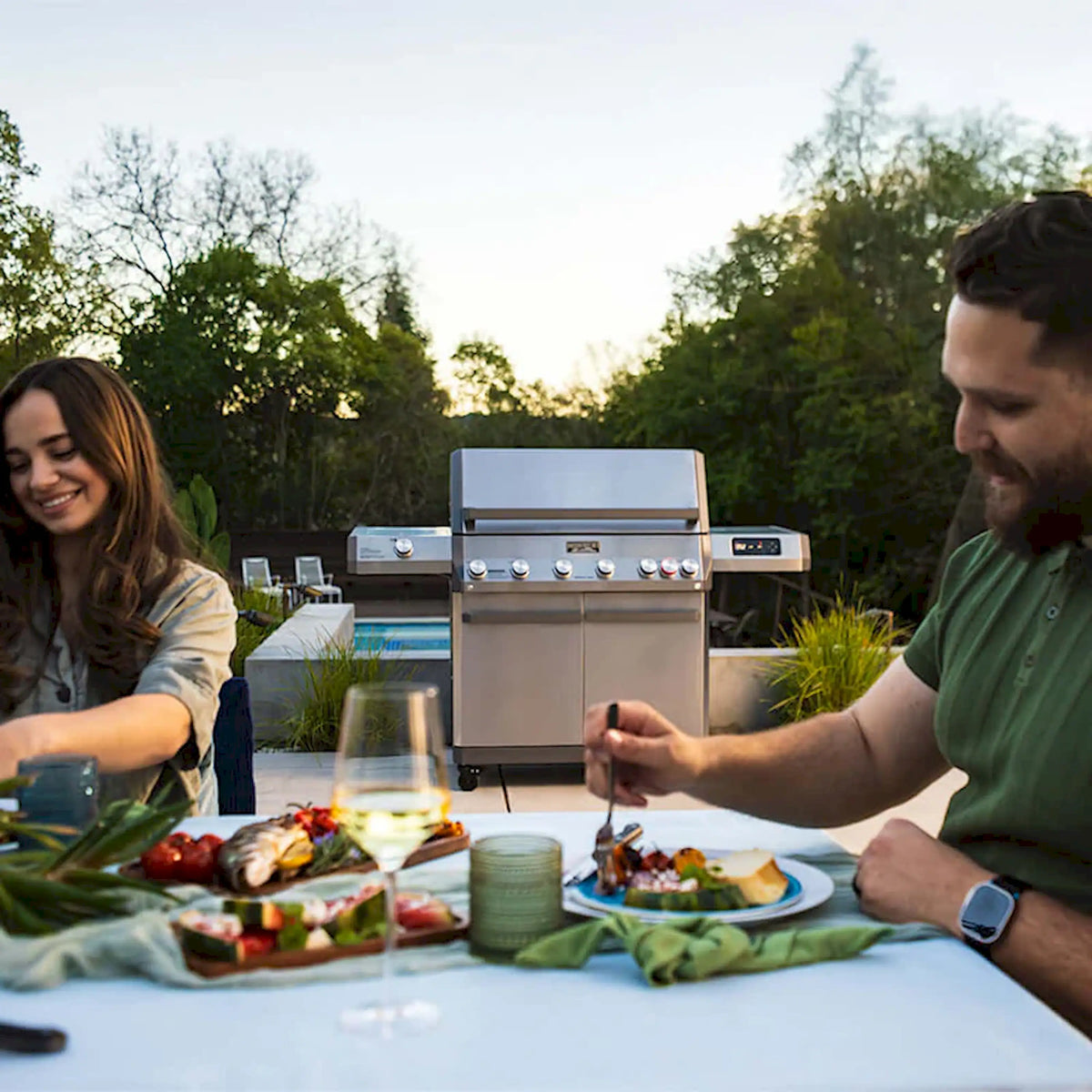 Outdoor stainless Monument gas grill on patio with people cooking at table