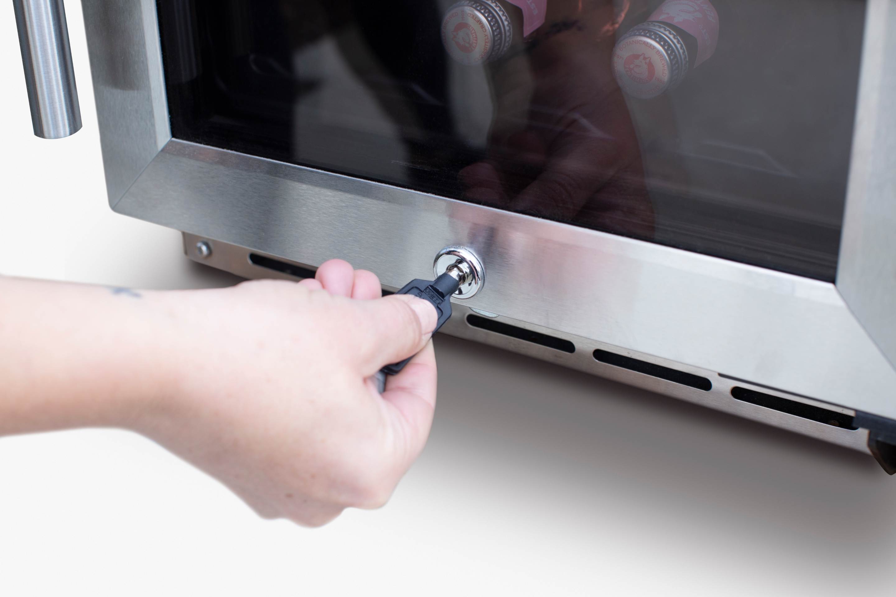 Hand adjusting wine cooler door latch on stainless frame with interior bottles