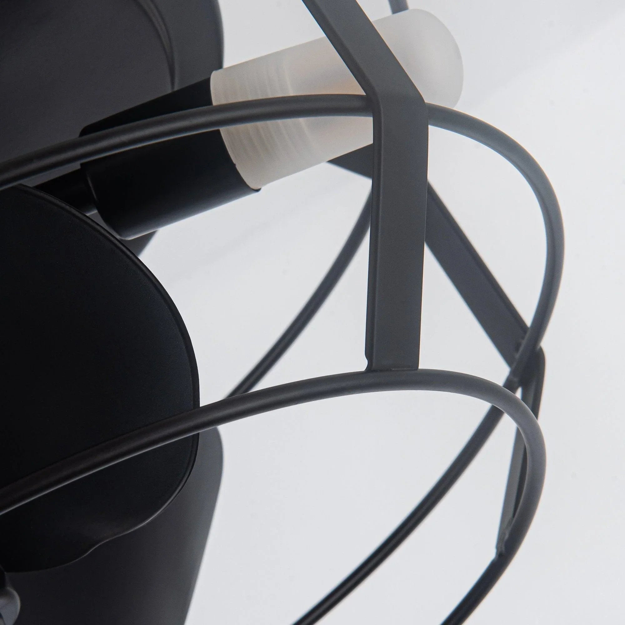 Close-up of black fan cage bars and blade housing under the ceiling light