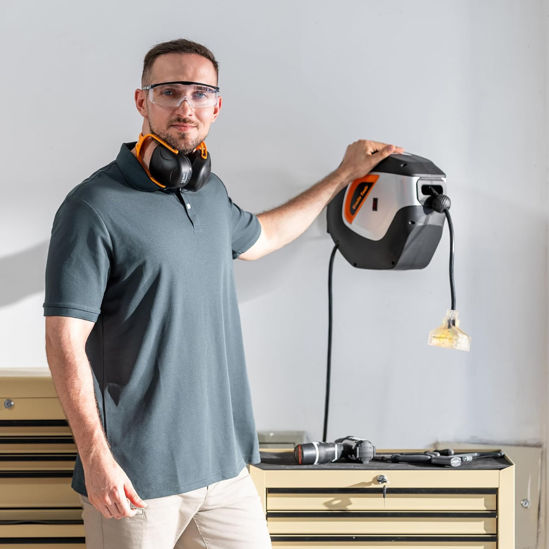 Retractable extension cord reel mounted overhead with power cord and plug hanging down, black body.