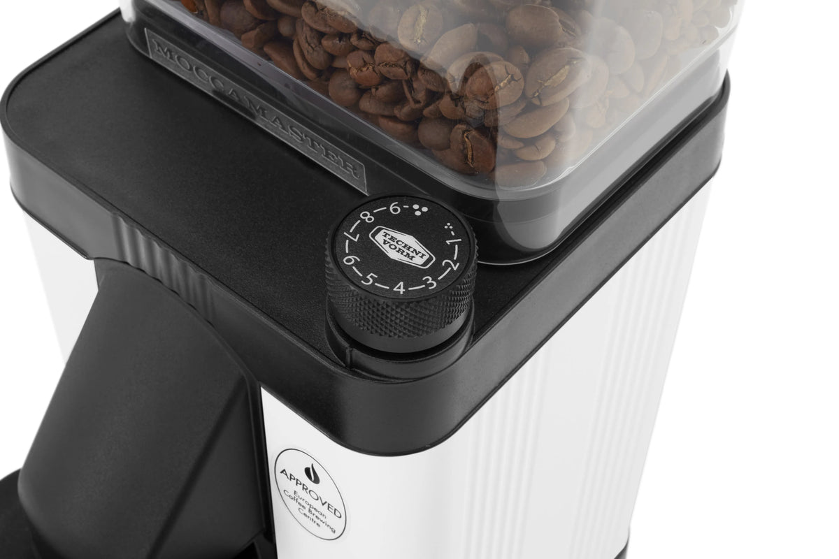 Matte white burr grinder top with bean hopper and black grind setting dial, close-up.
