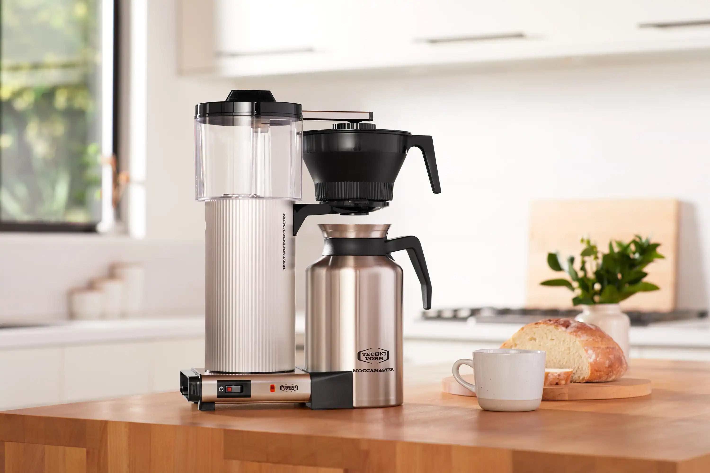 Brushed silver coffee maker with transparent tank, black funnel, and metal carafe