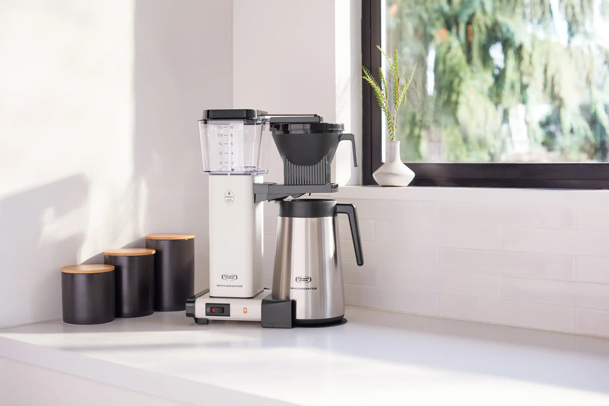 Moccamaster off-white coffee maker with thermal carafe and black side handle on counter