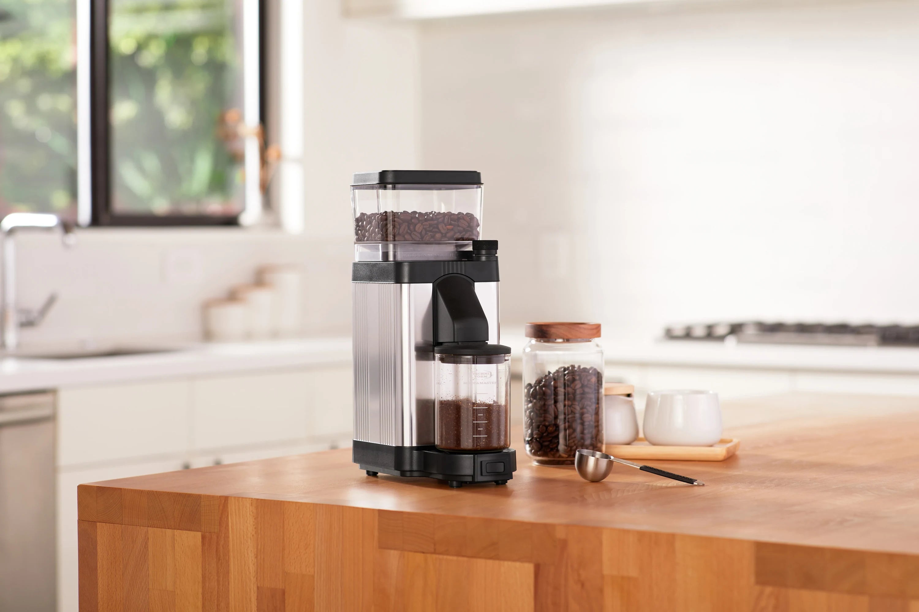 Polished silver burr coffee grinder with black base and transparent hopper