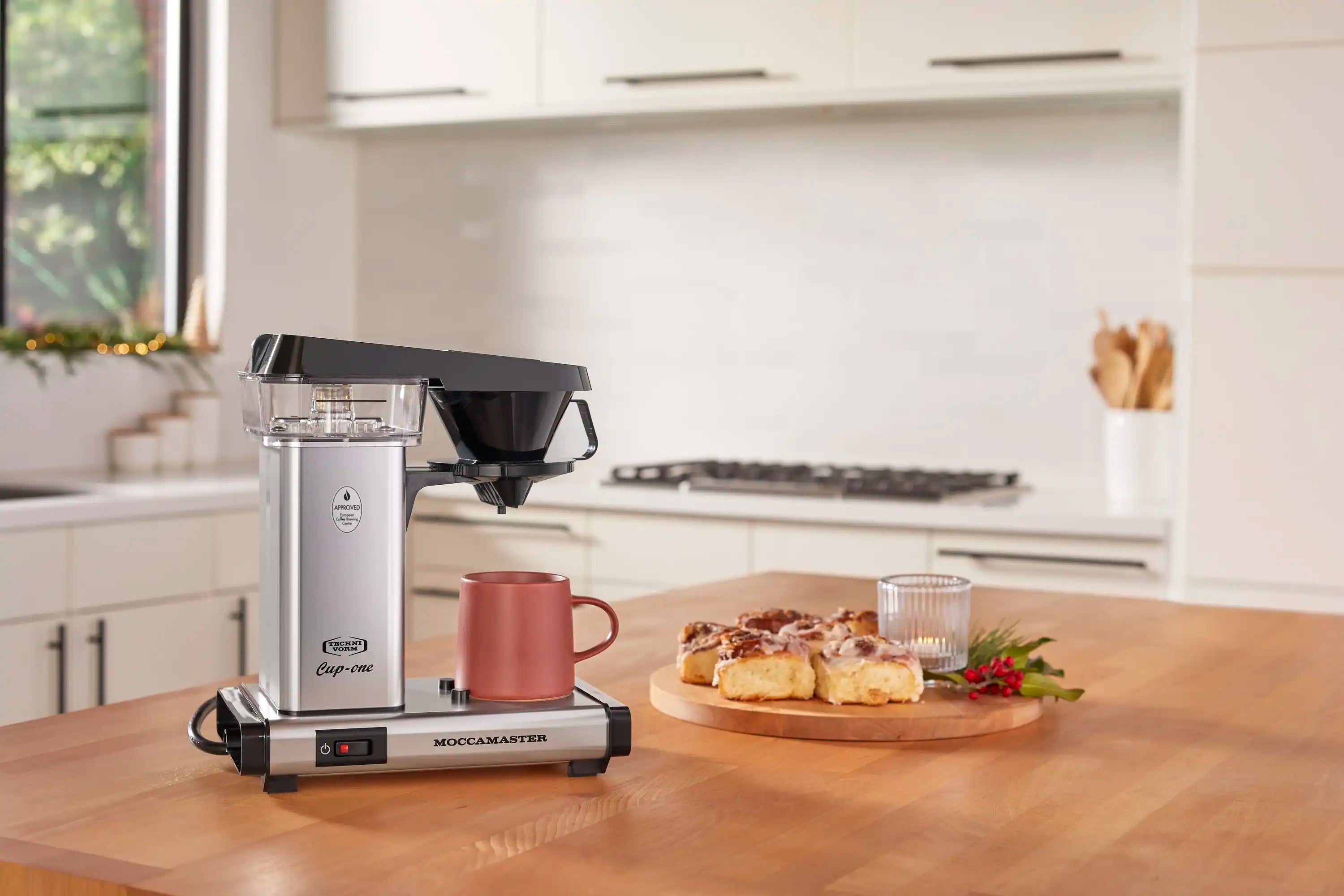 Single-cup coffee maker in polished silver with black funnel on countertop