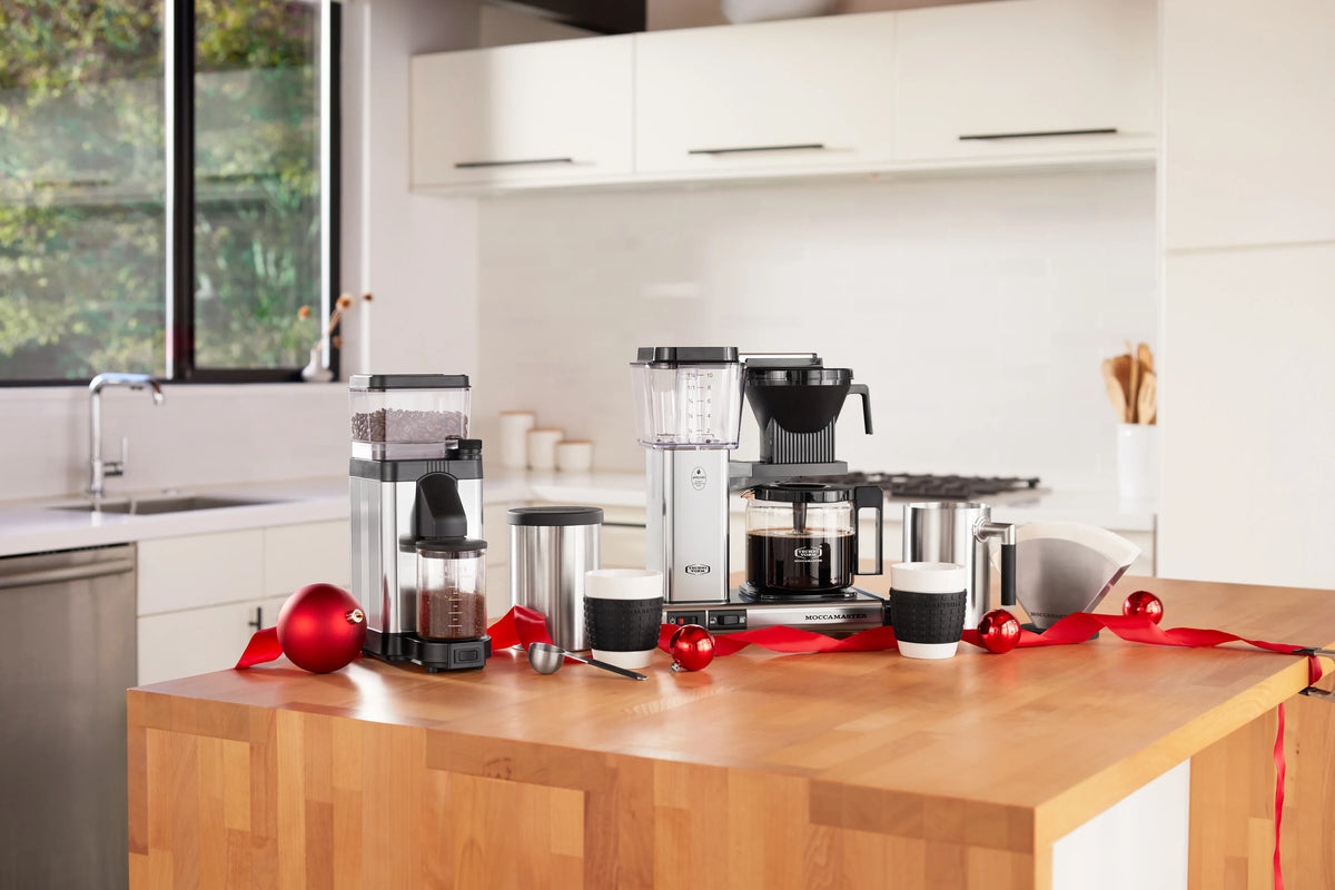 Polished silver burr grinder with clear hopper and black grinding spout on counter