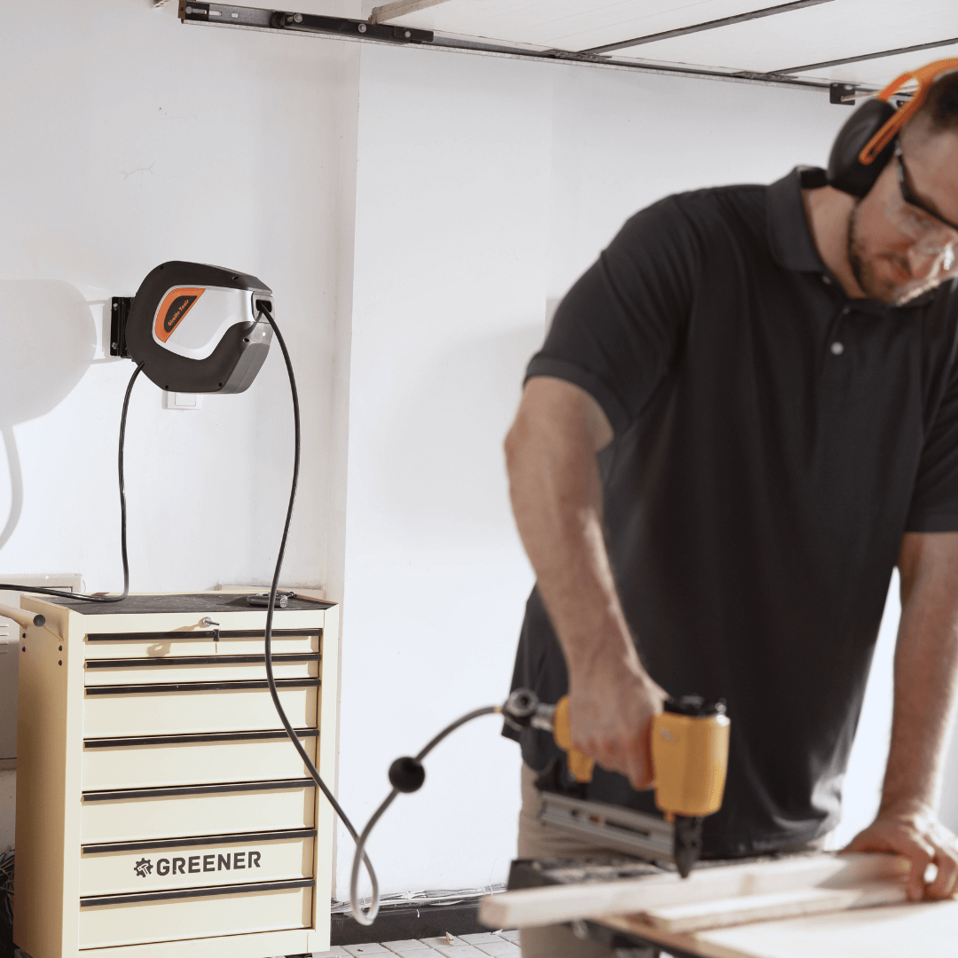 Retractable extension cord reel with cord connected, in use near workbench, black and orange panel.