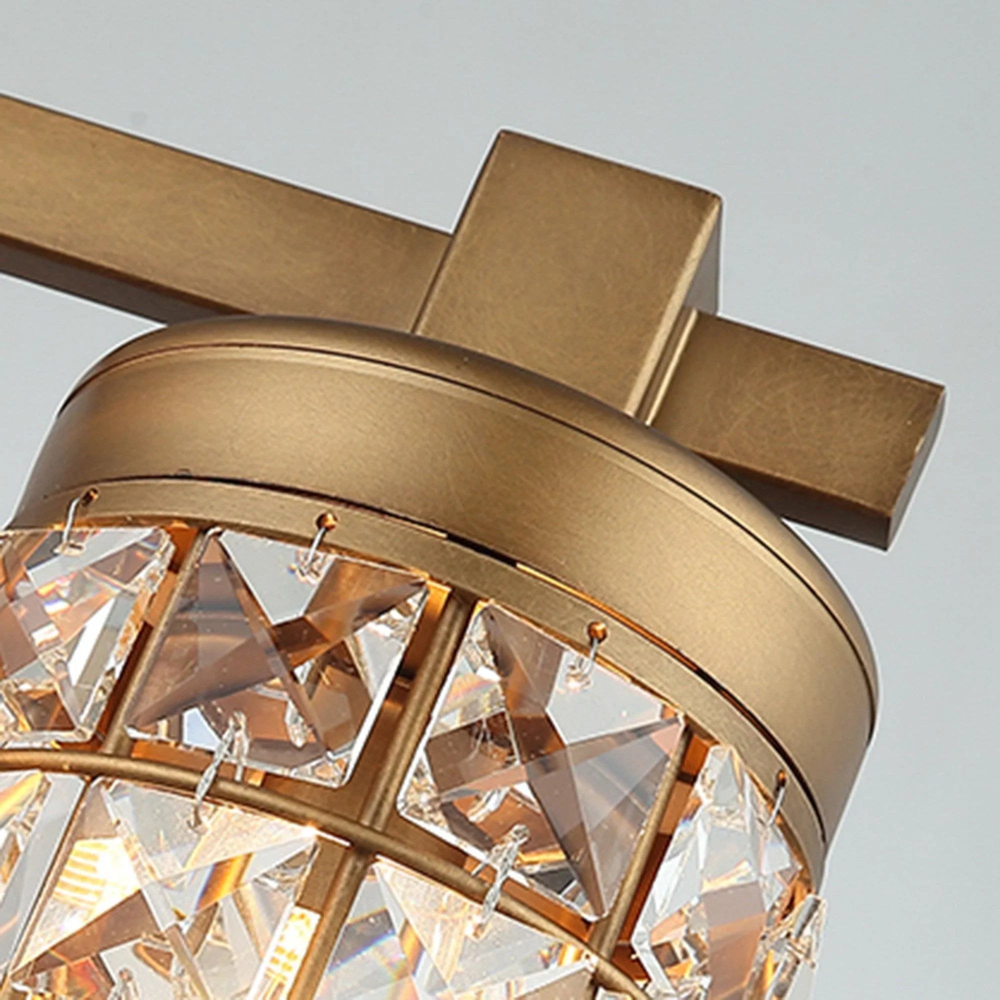 Golden cylindrical vanity light shade with faceted crystal and metal top cap, close-up