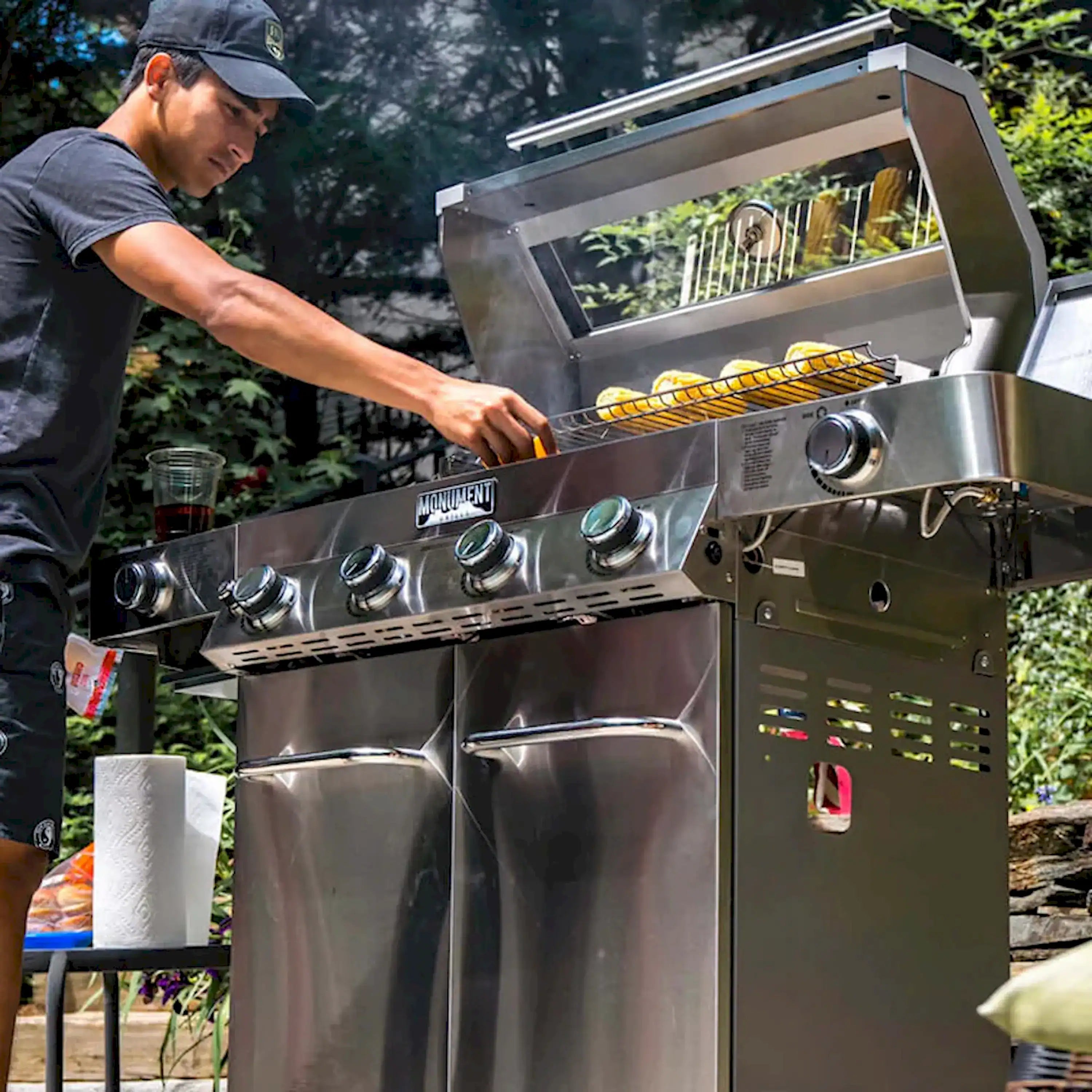Man using tongs to grill food on grates in a stainless steel propane grill