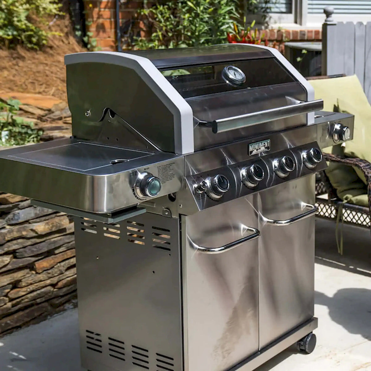 Stainless steel 4-burner propane grill with side tray, handles, and control knobs