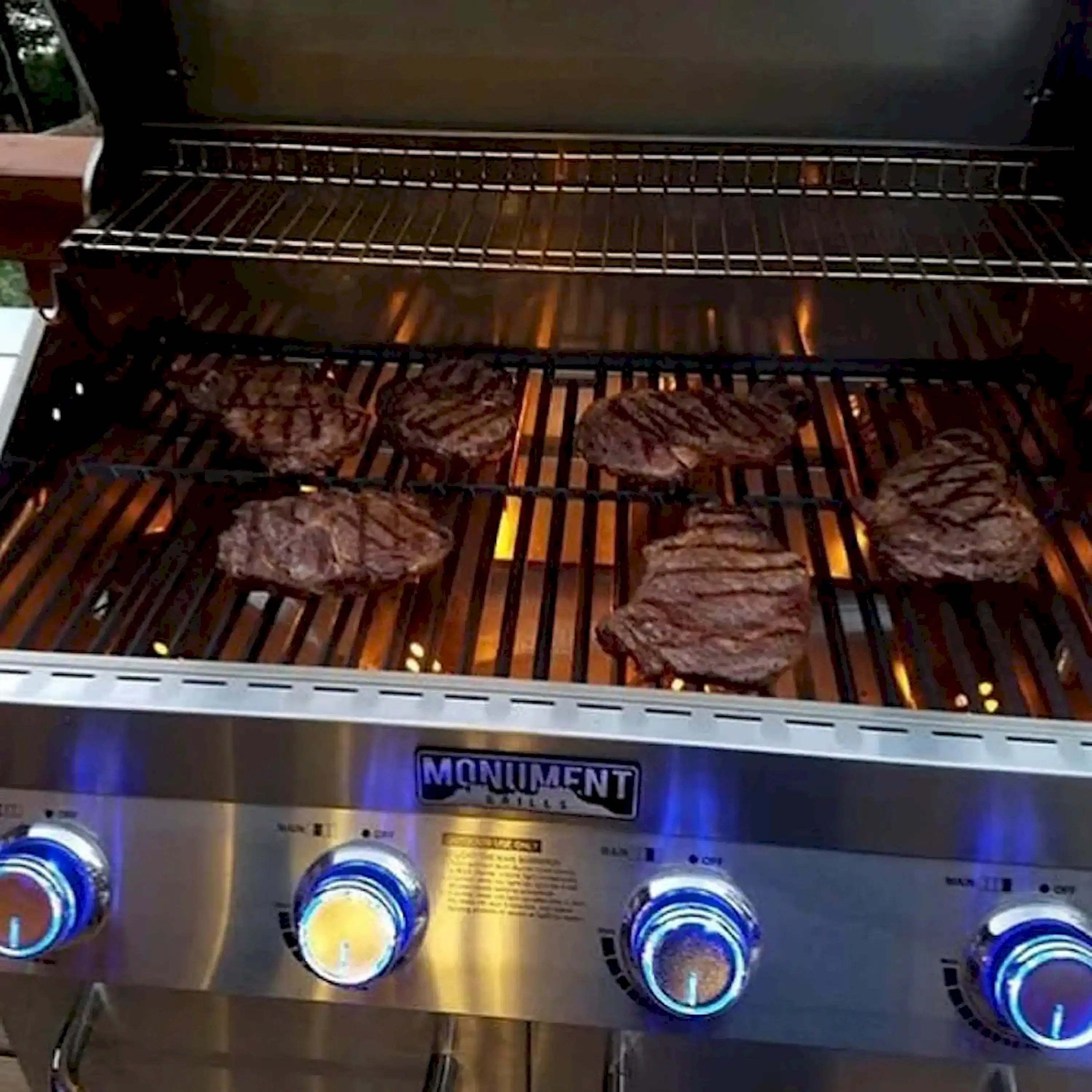 Burgers grilling on dark grates inside stainless steel barbecue hood