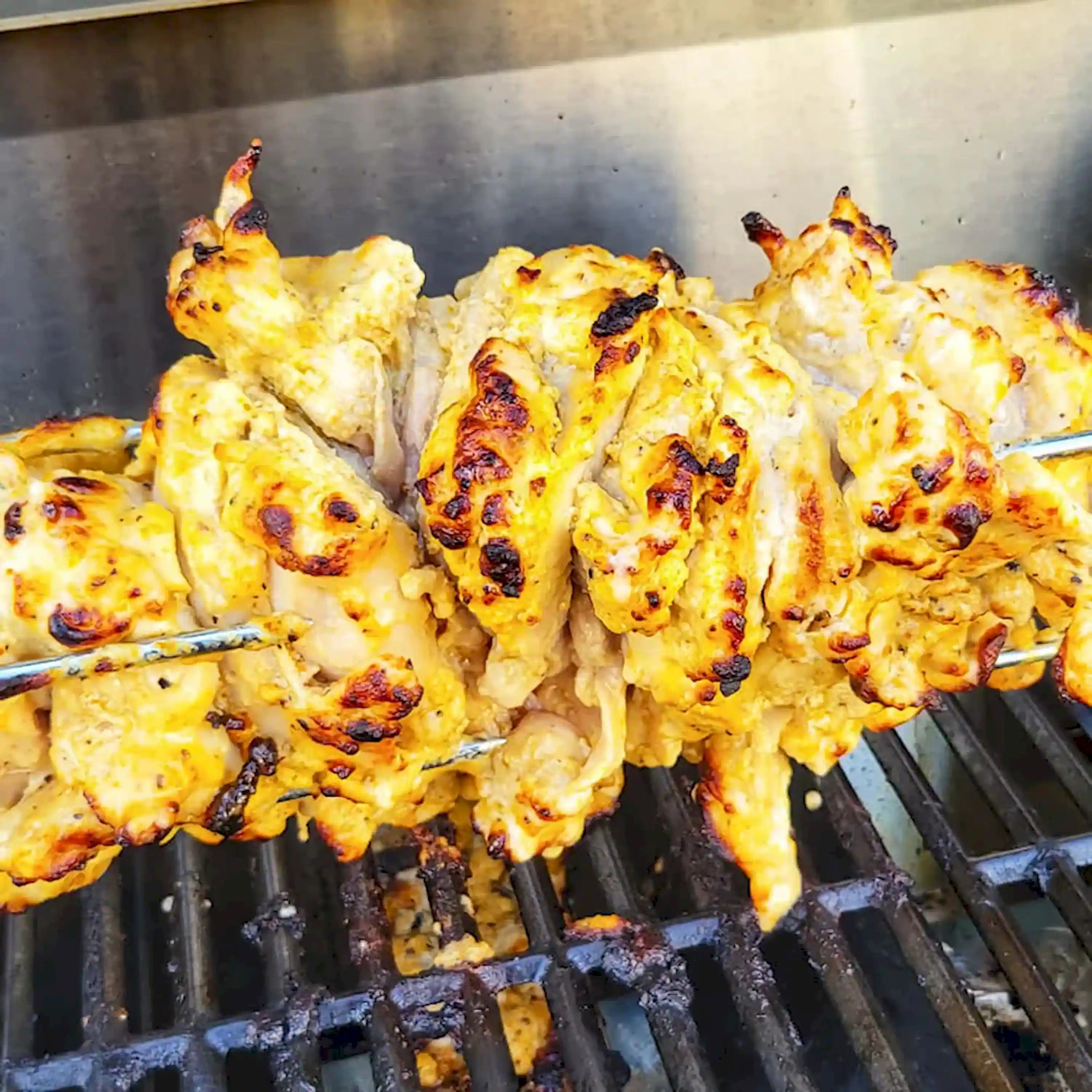 Grilled chicken pieces on black cast-iron grill grates inside the propane grill