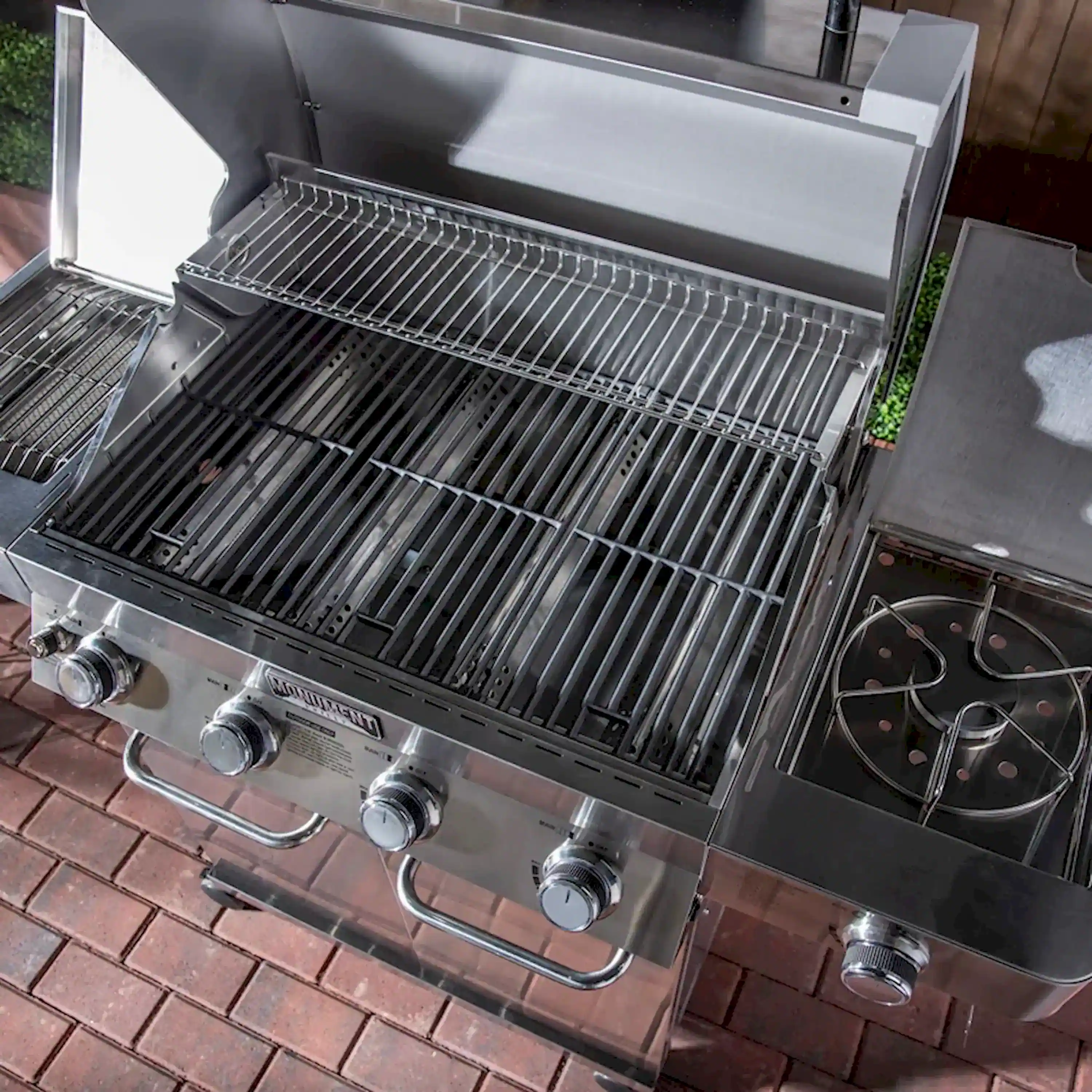 Stainless steel grill with open lid and cooking grates over black warming surface