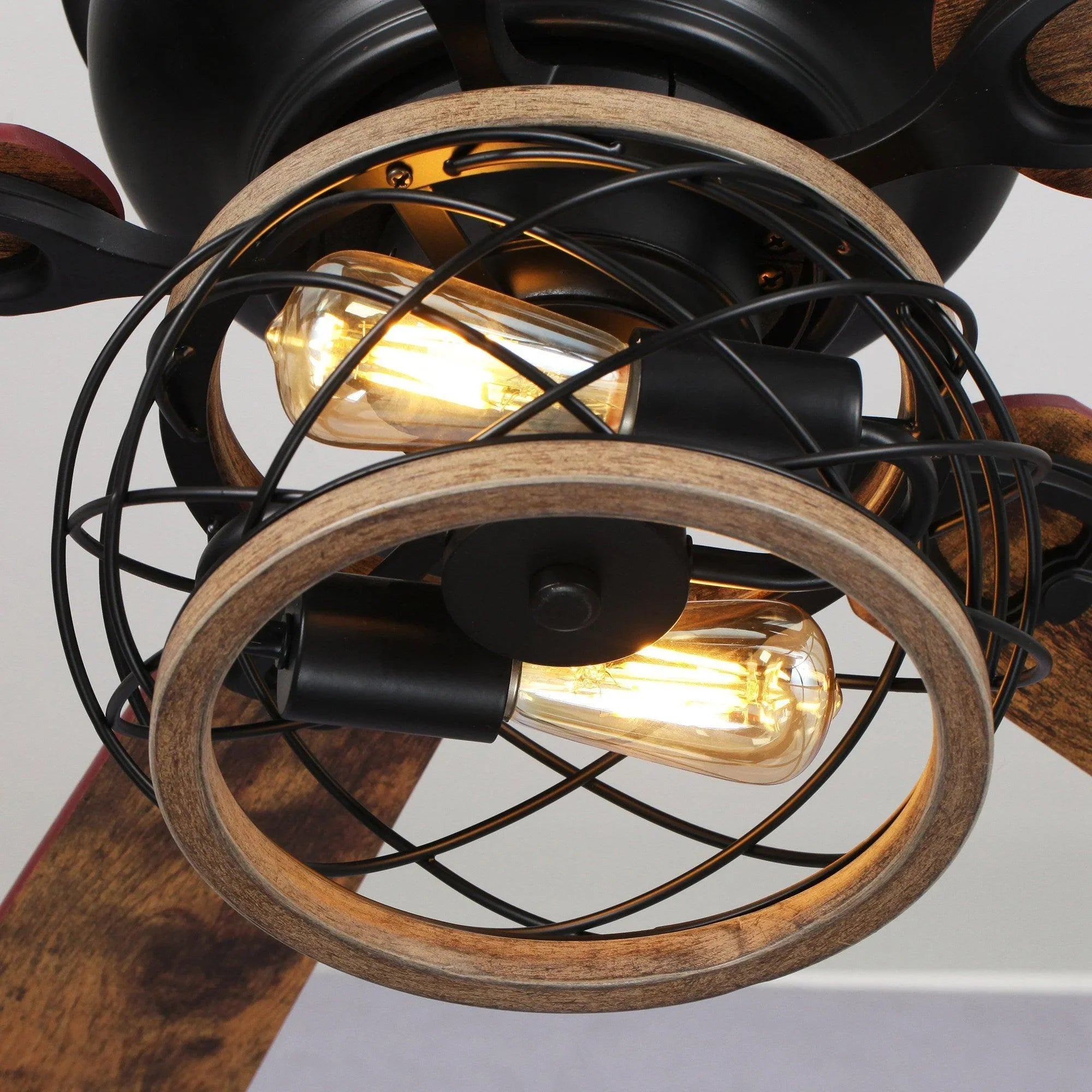 Close-up of black caged light with two glowing bulbs and wood trim ring on ceiling fan