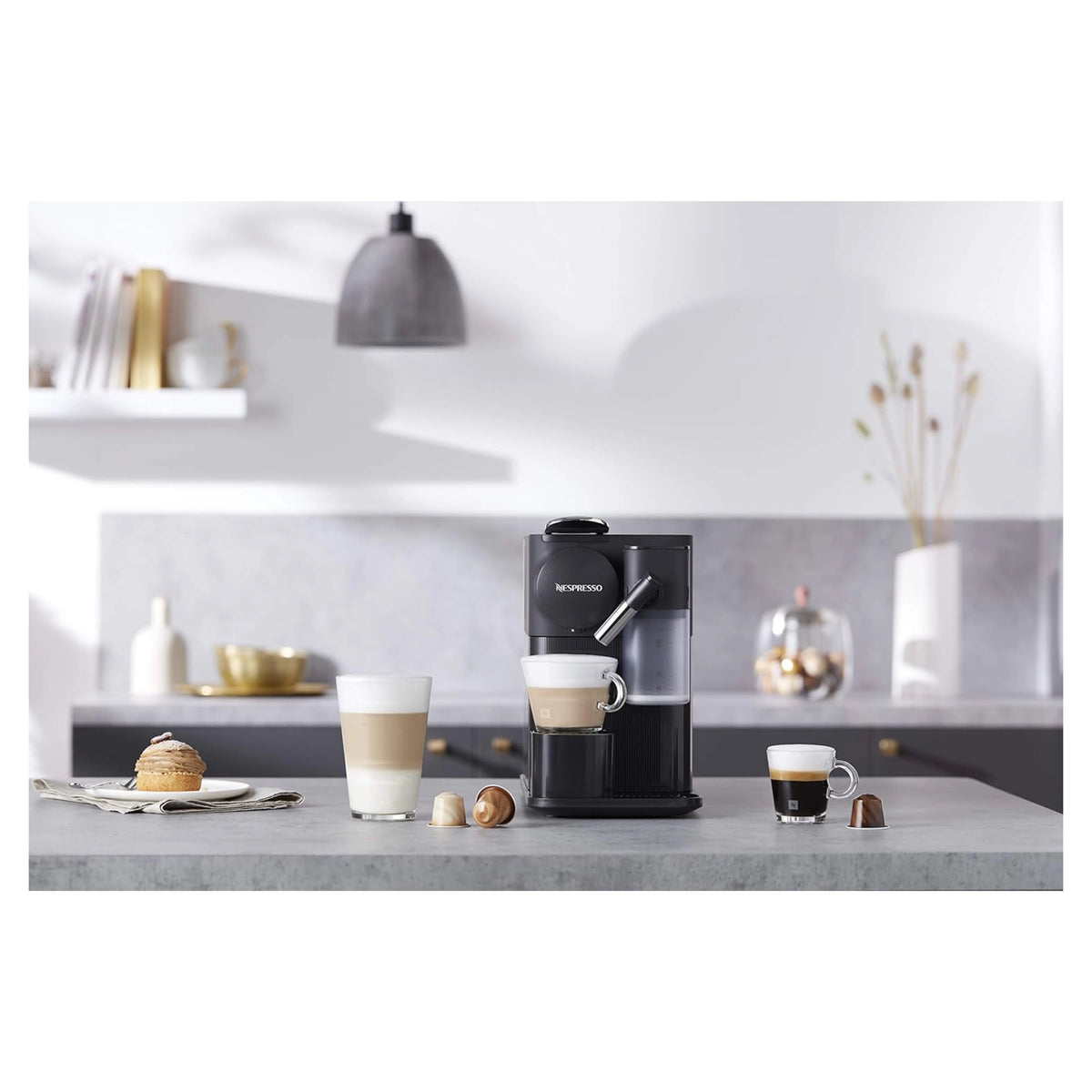 Black Nespresso espresso machine on countertop with cups and froth pitcher nearby