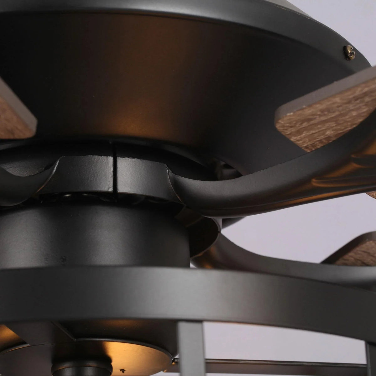 Close-up of black ceiling fan motor housing and curved blade arms with wood blades