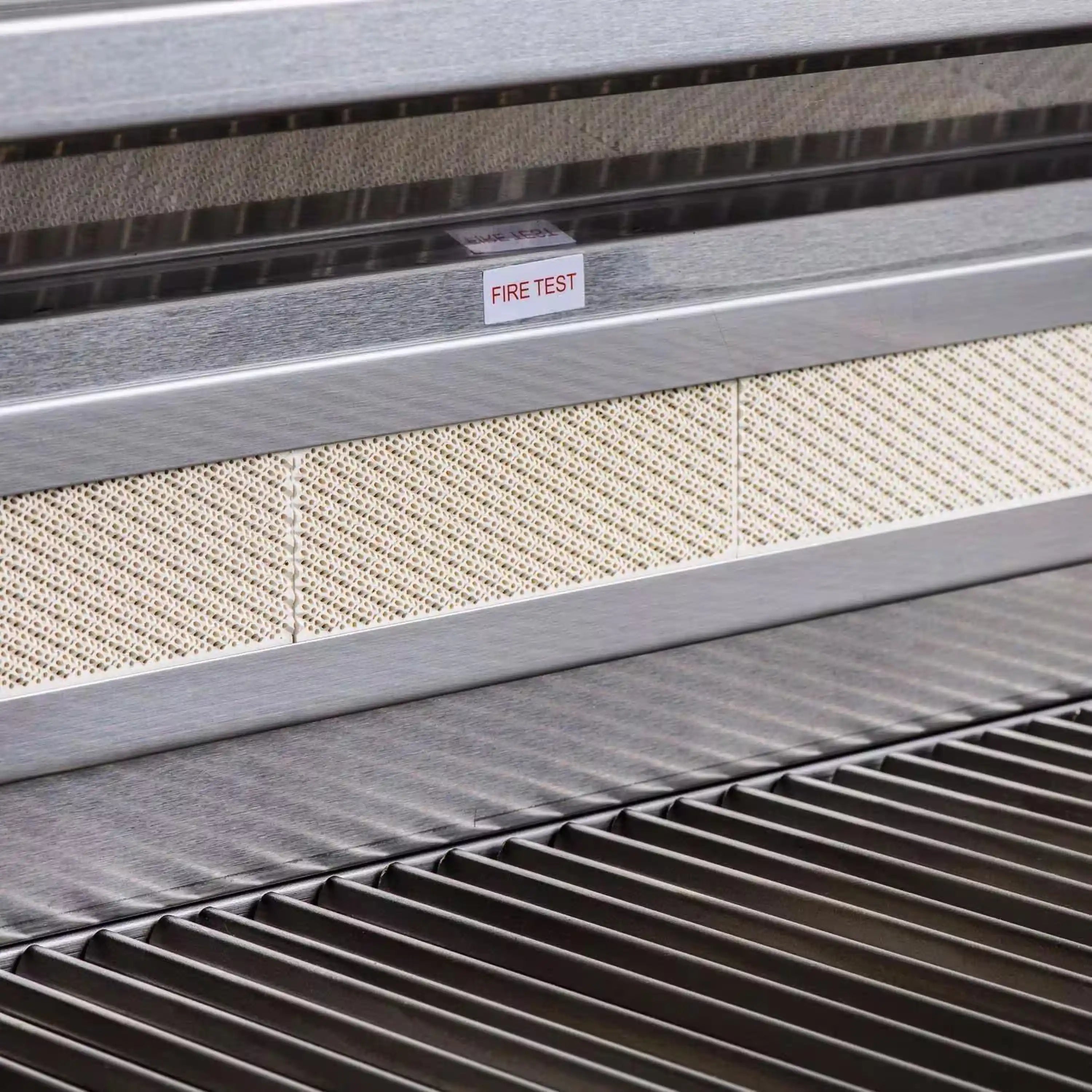 Stainless grill interior with metal tray and mesh shield labeled 'FIRE TEST'