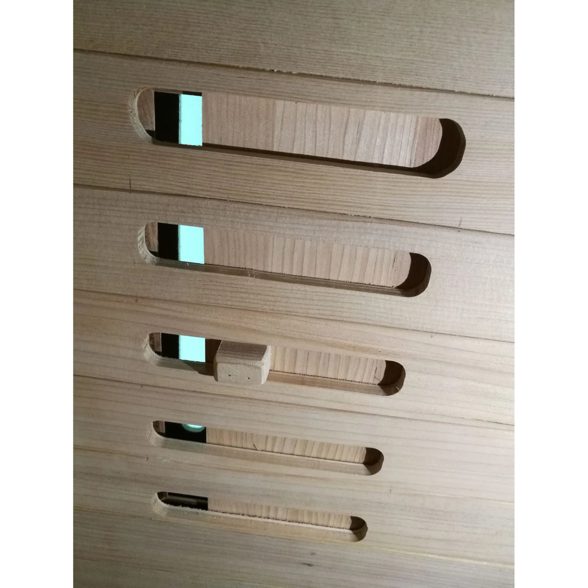 Row of vent-like openings with blue LED glow on a light wood sauna wall.