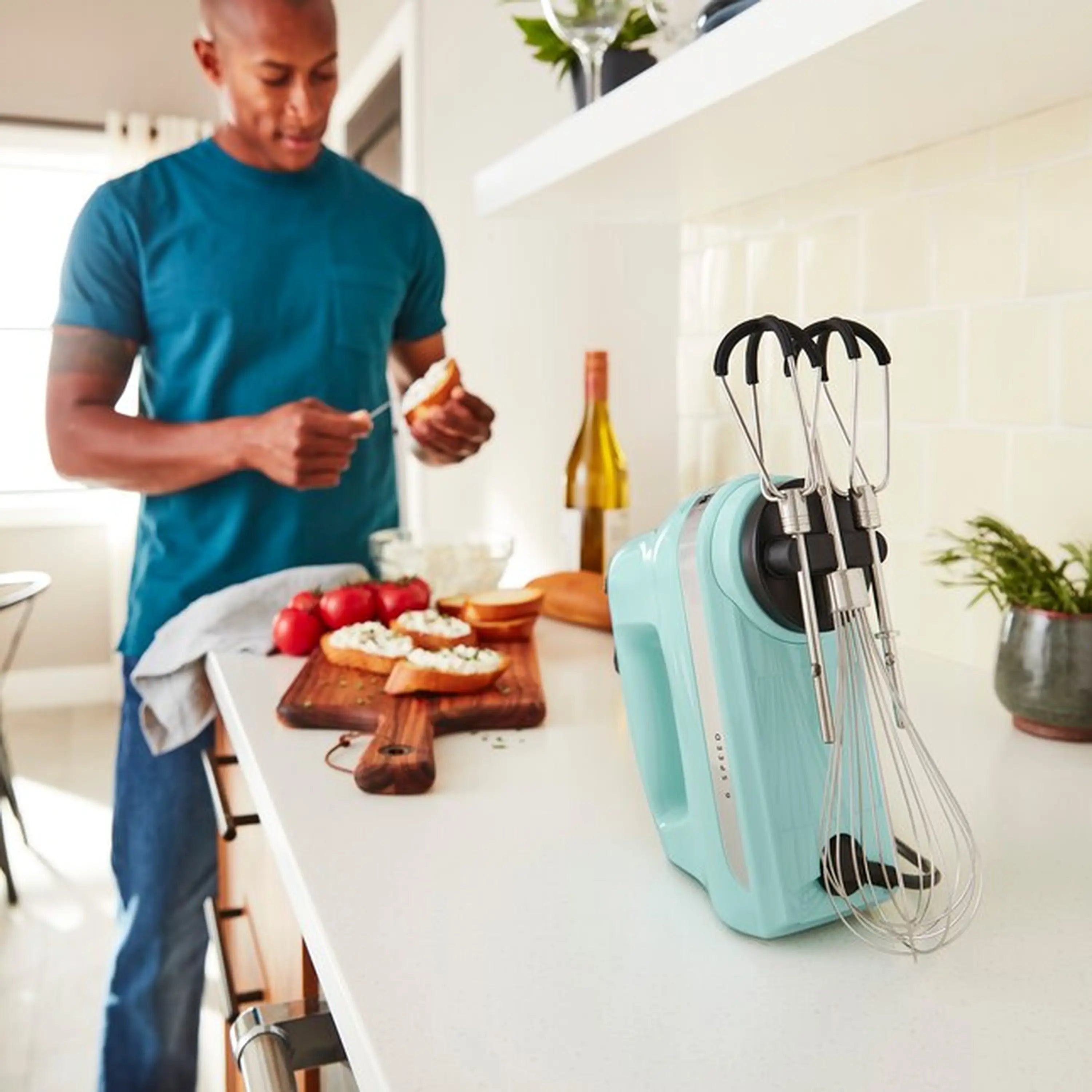 Ice blue hand mixer with wire beaters standing upright on countertop