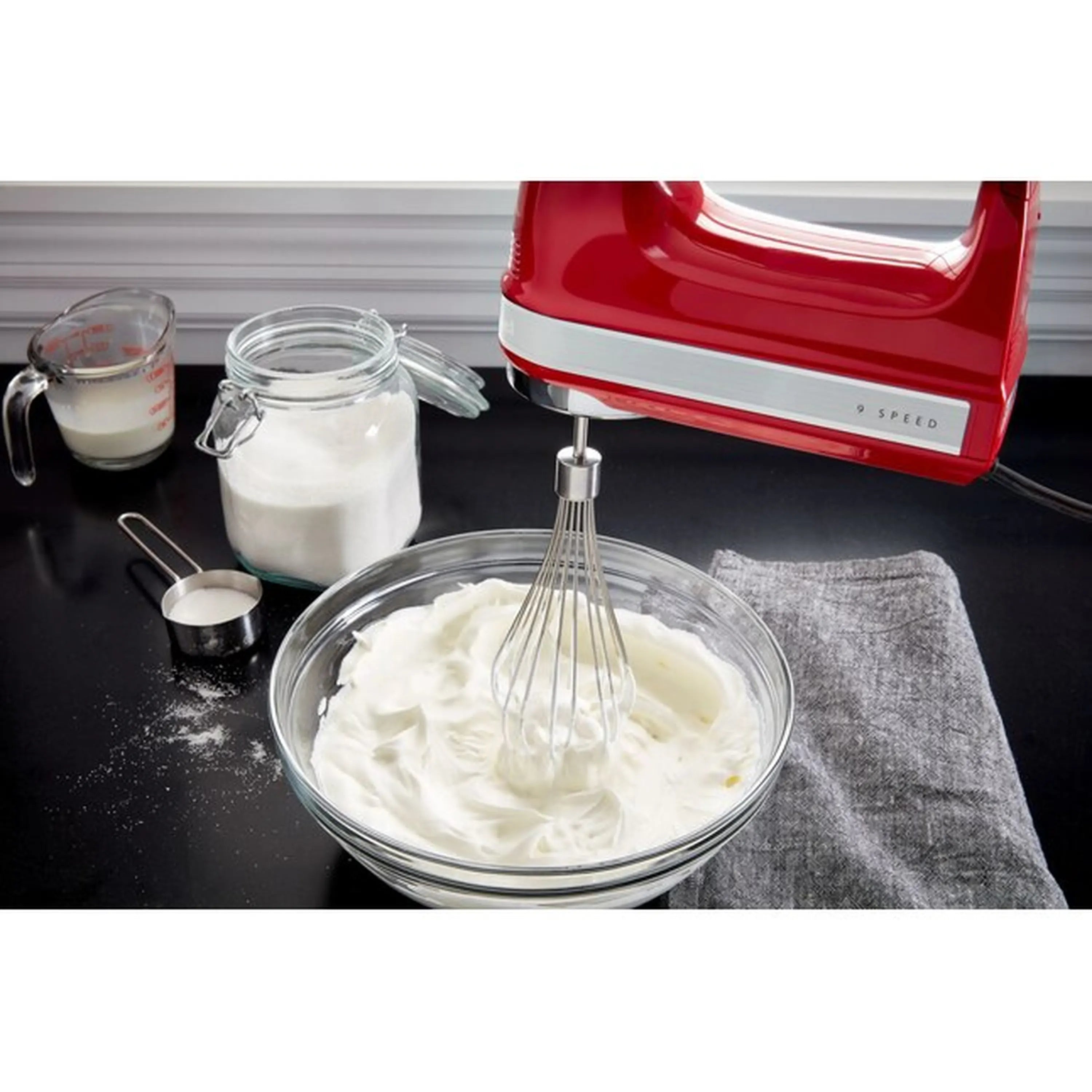 KitchenAid hand mixer whipping white cream in a glass mixing bowl