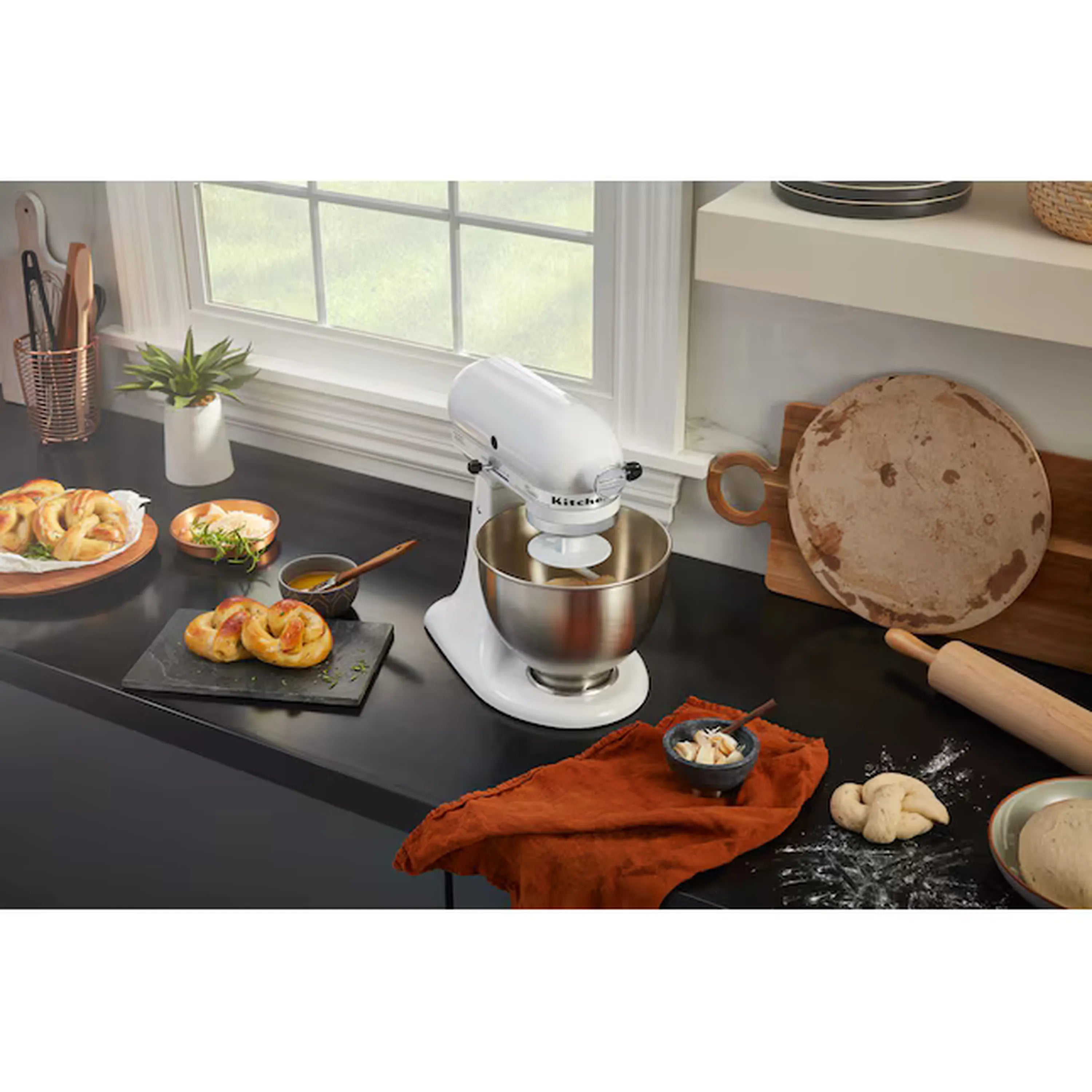 White tilt-head stand mixer with stainless bowl on dark countertop