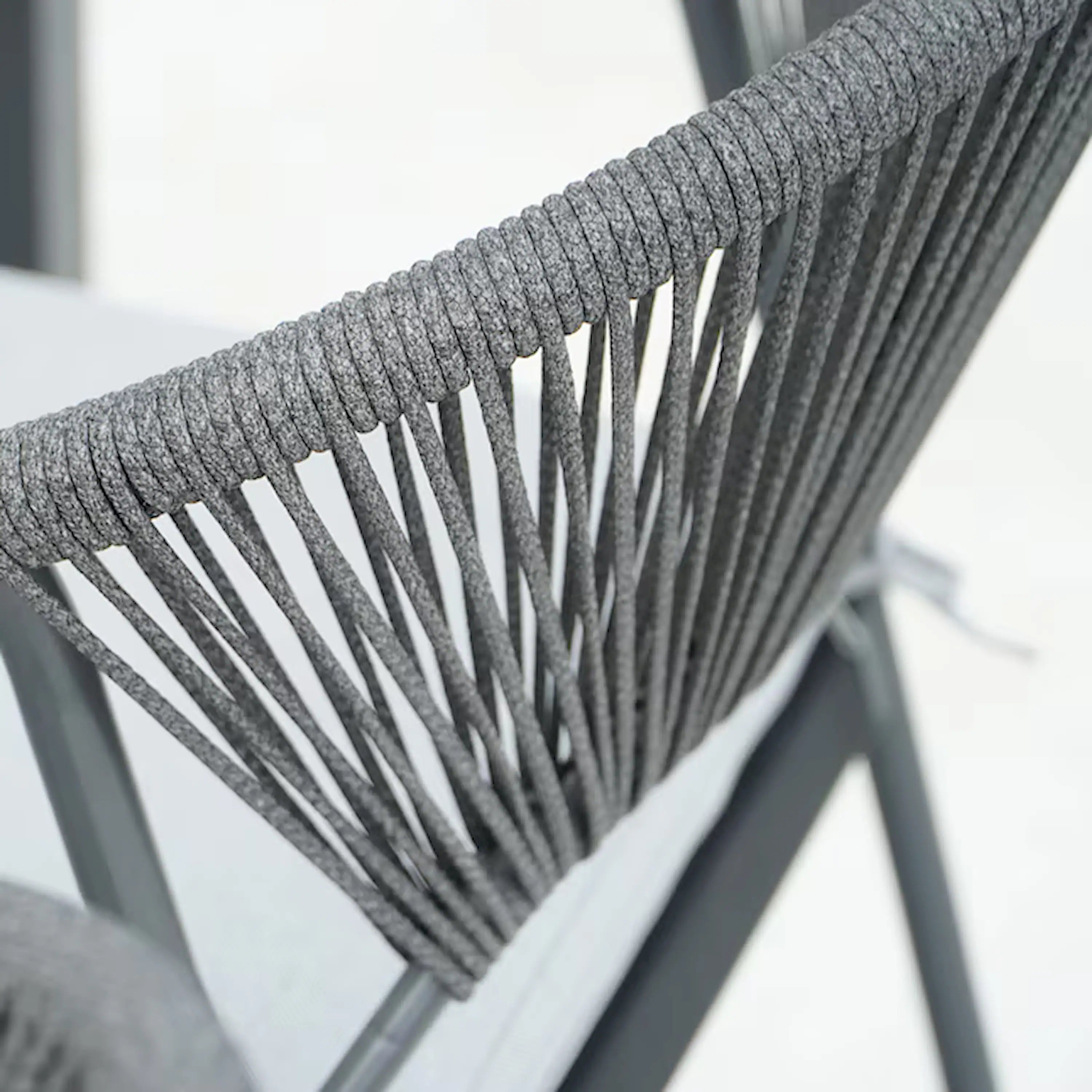 Outdoor dining chair back with gray rope weave and black metal arm frame, close-up.