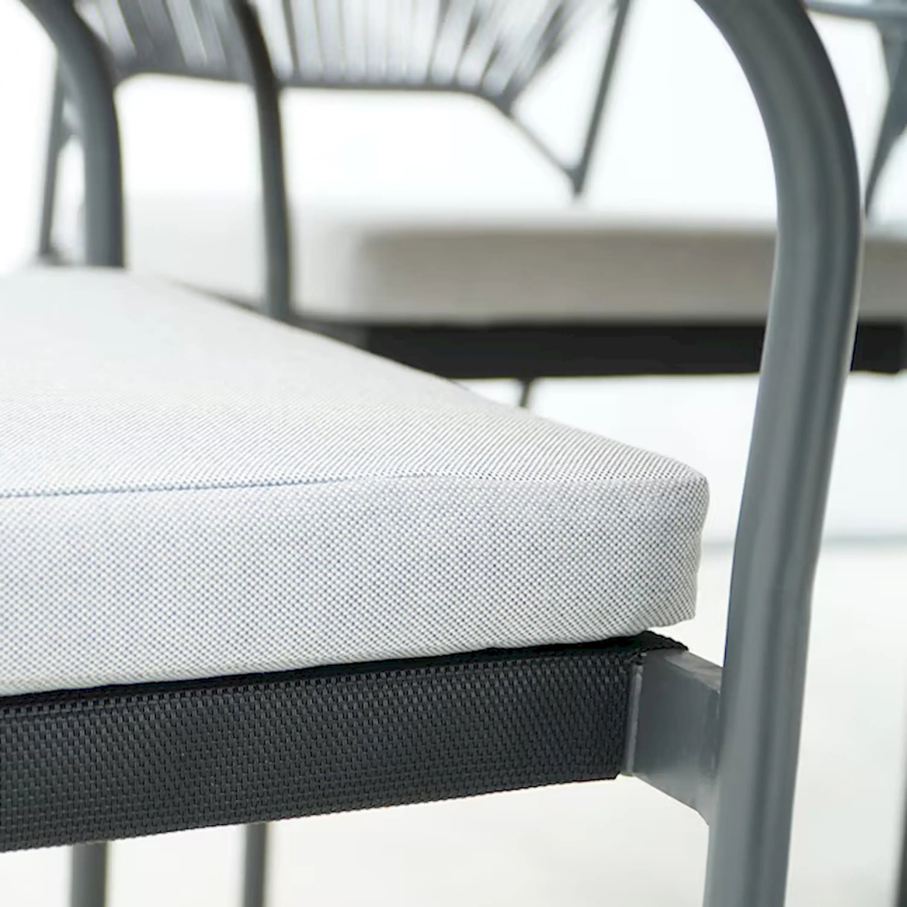 Outdoor dining chair seat cushion on black woven frame, close-up of cushion edge.
