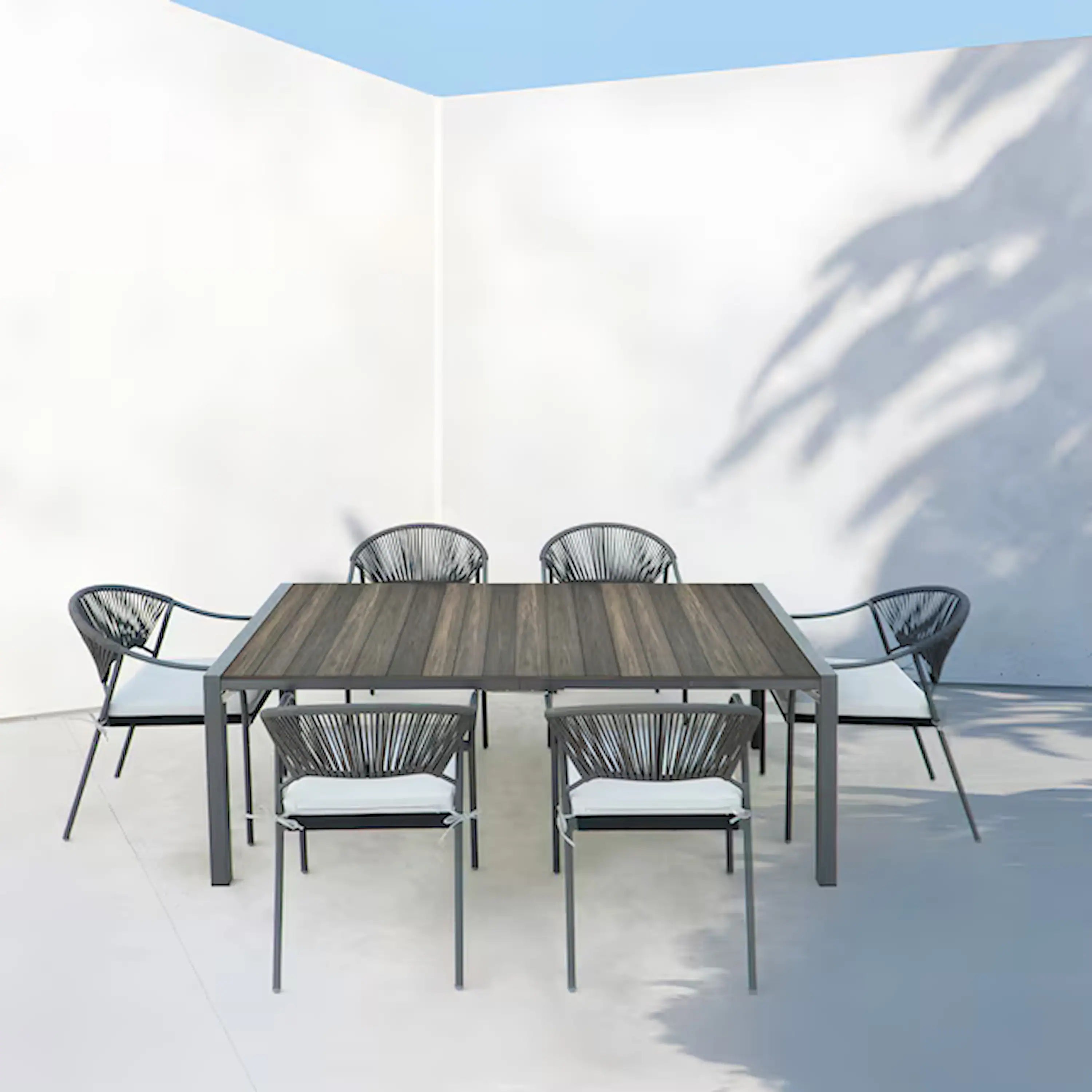 Outdoor patio dining set with rectangular table and six chairs with black rope backs.