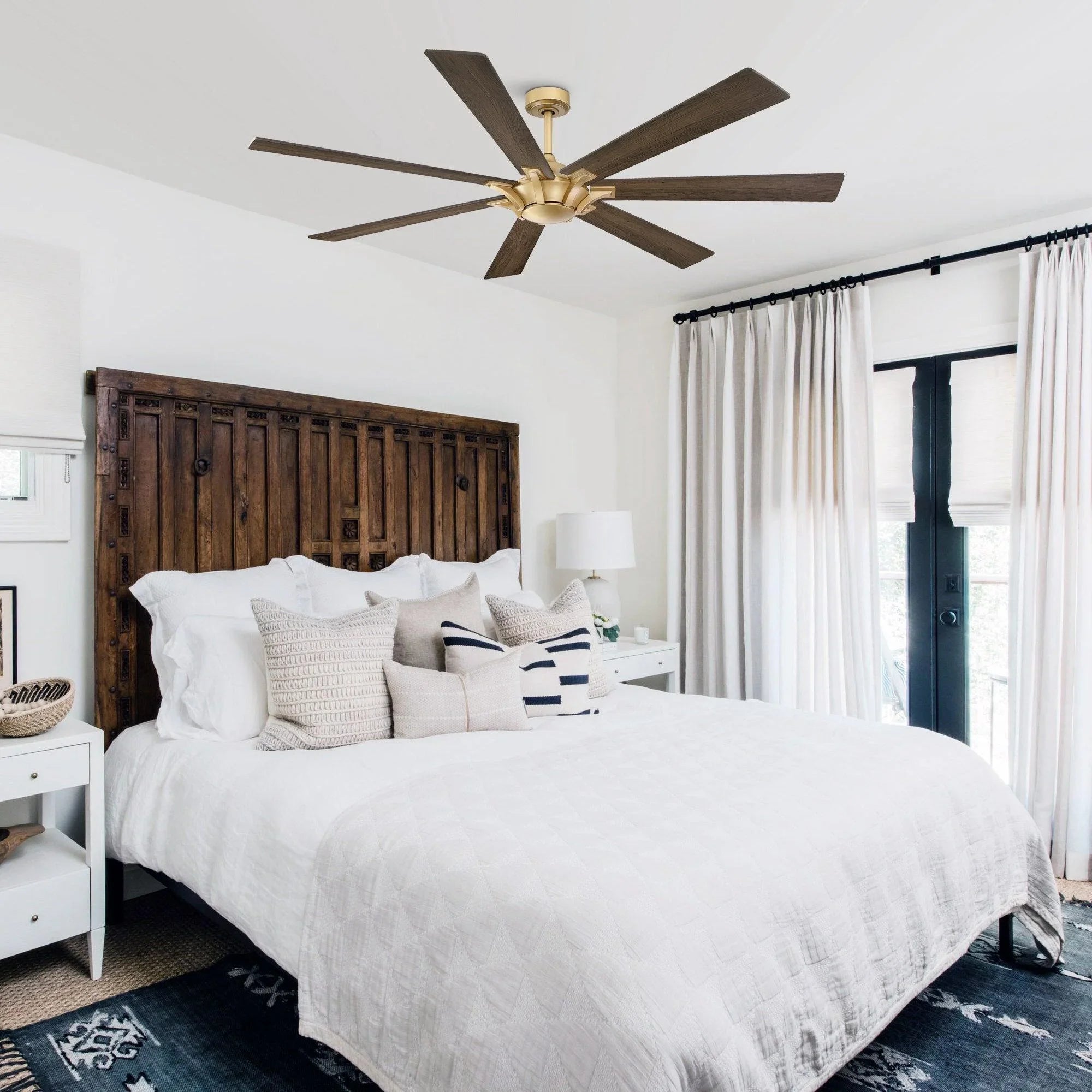 Golden ceiling fan with five wood blades above a bedroom bed