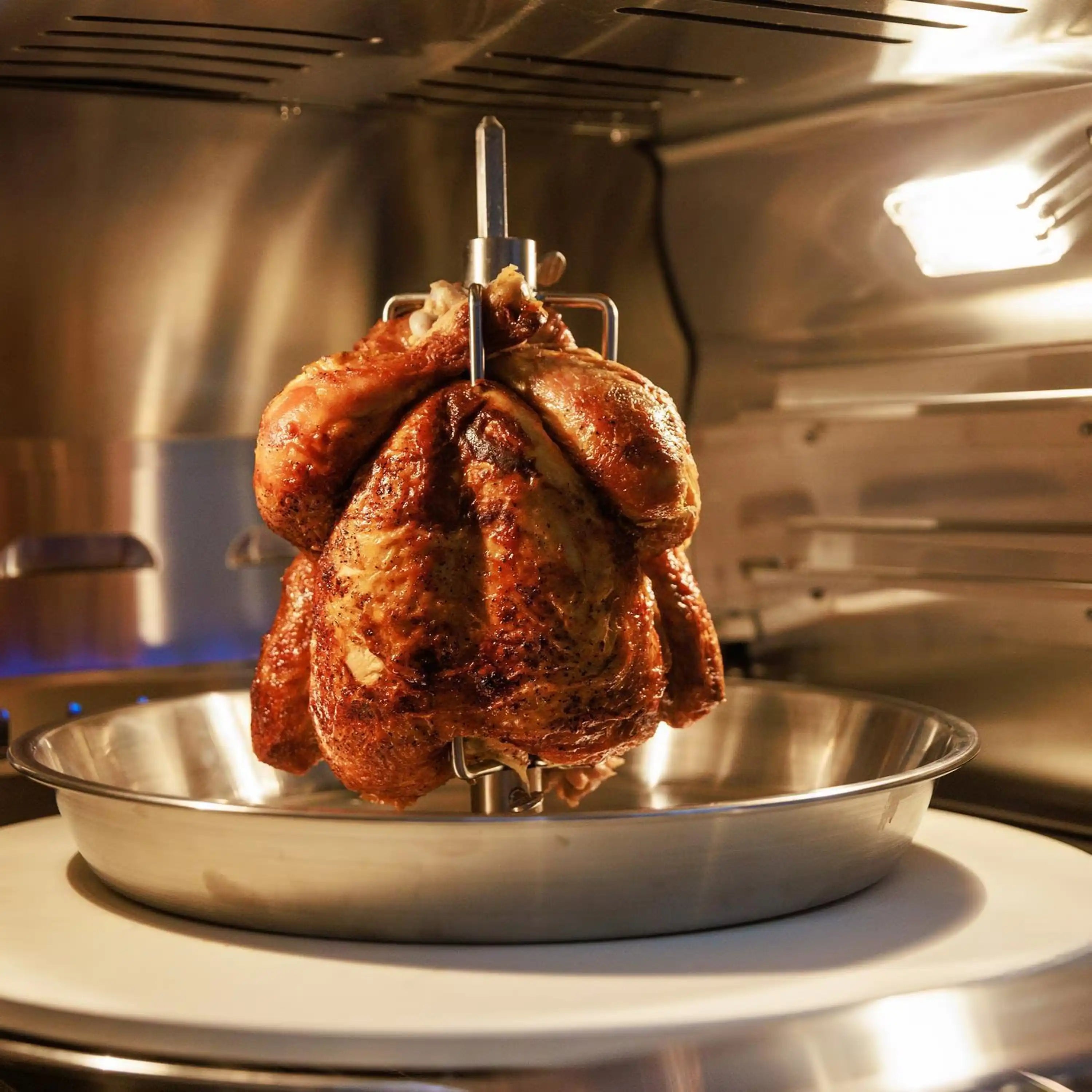 Countertop propane pizza oven with rotisserie chicken on metal tray in cooking chamber