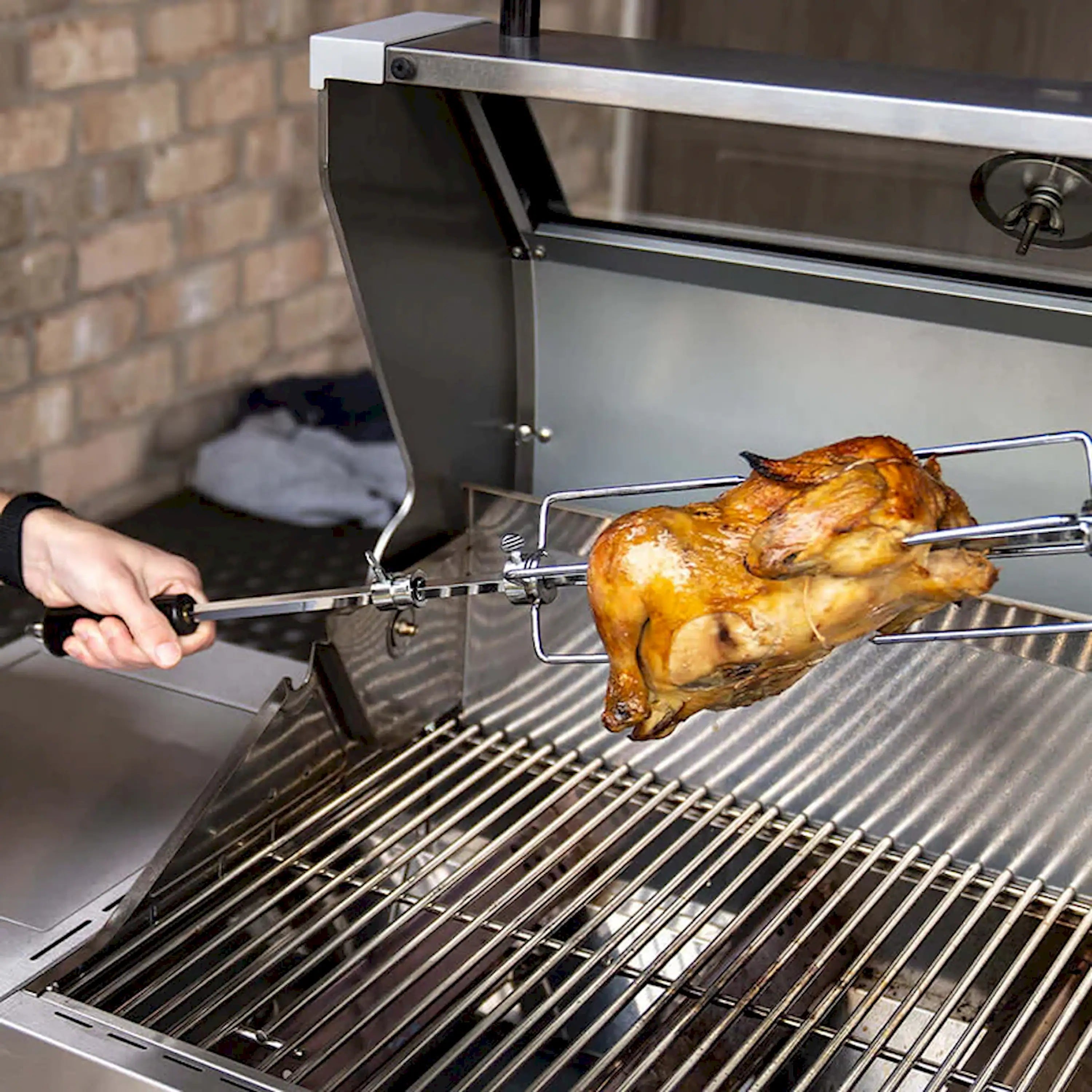 Rotisserie spit and forks holding whole roasted chicken on stainless grill grates