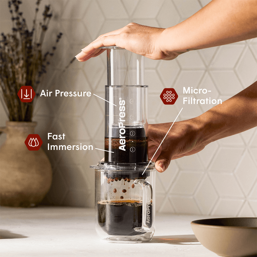 Clear AeroPress coffee maker in use: purple chamber pressed into a clear mug