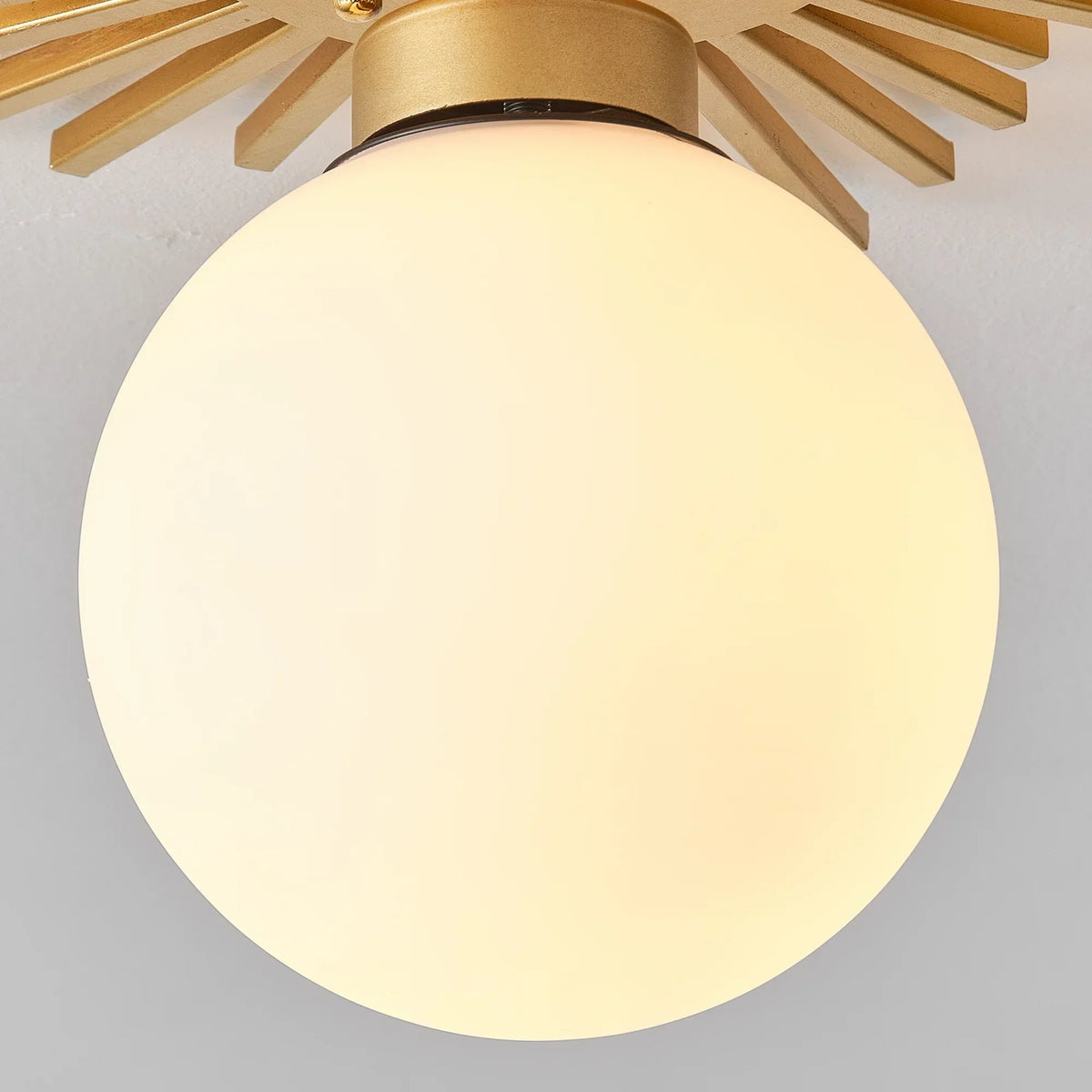 Golden flush-mount ceiling light with frosted globe shade and radial metal rays