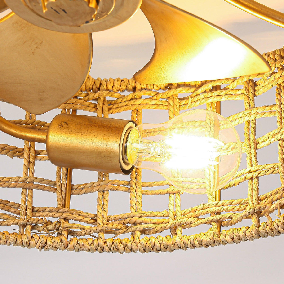 Close-up of golden fan blades and glowing bulb inside woven rattan housing.
