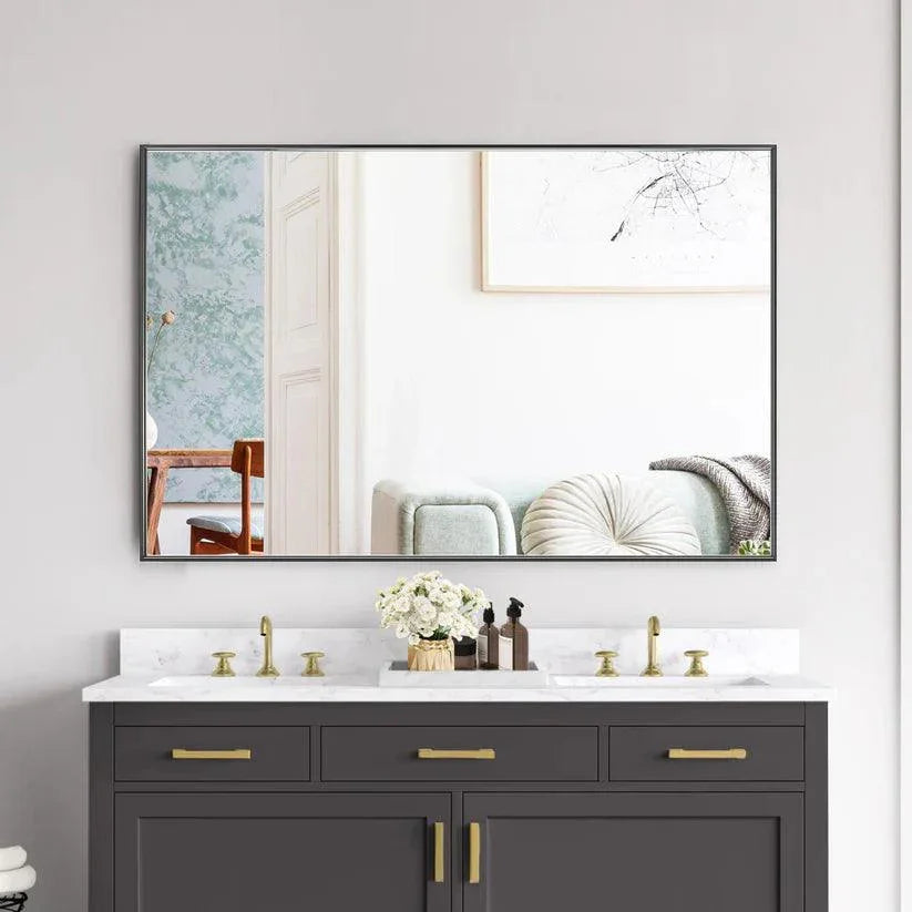 Rectangular wall mirror with black frame above a dark dresser with gold hardware.