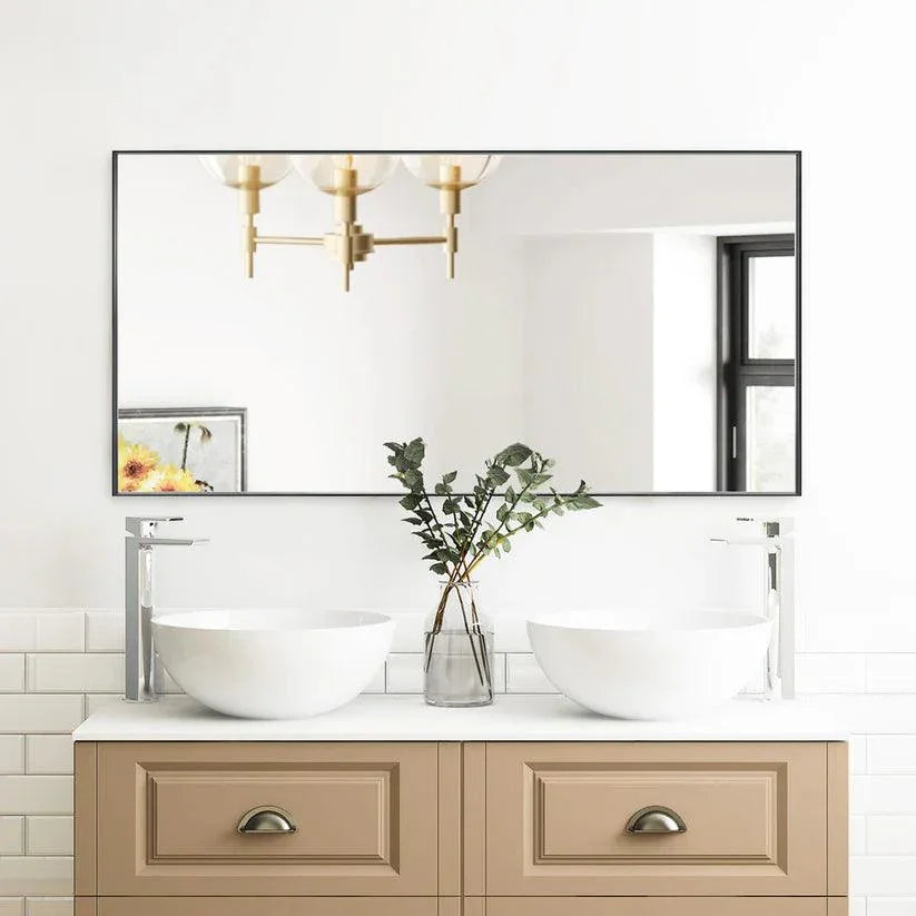 Rectangular wall mirror with gold aluminum frame above a light vanity with drawers.