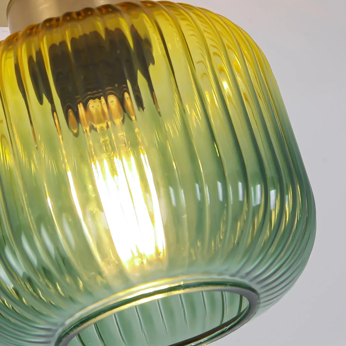 Ribbed green striped glass shade with glowing bulb in brass semi-flush mount