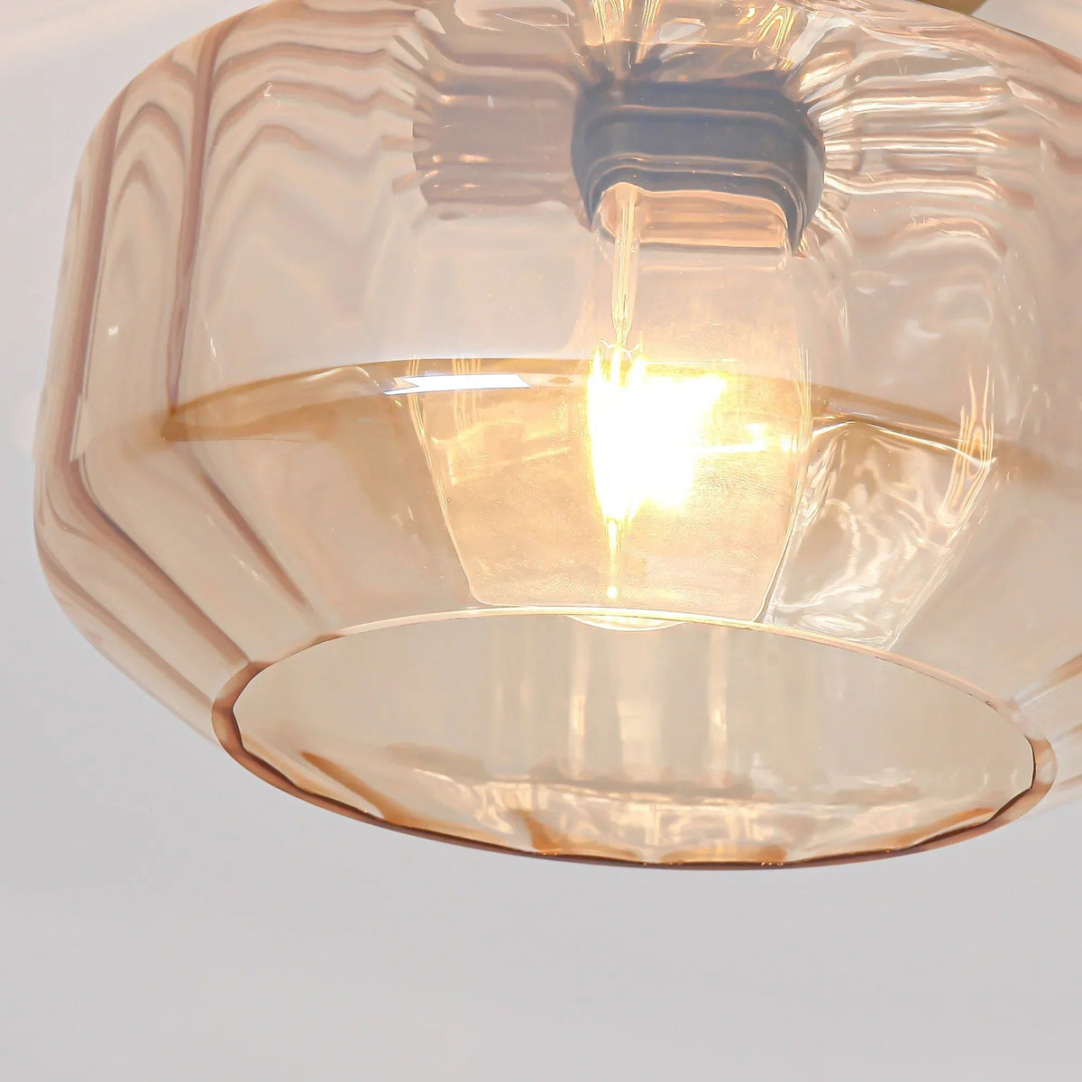 Clear faceted glass shade and glowing exposed bulb under a golden ceiling canopy