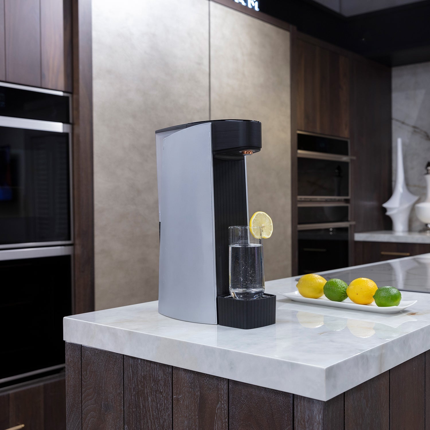 Silver and black sparkling water maker on a kitchen counter with a glass of bubbles