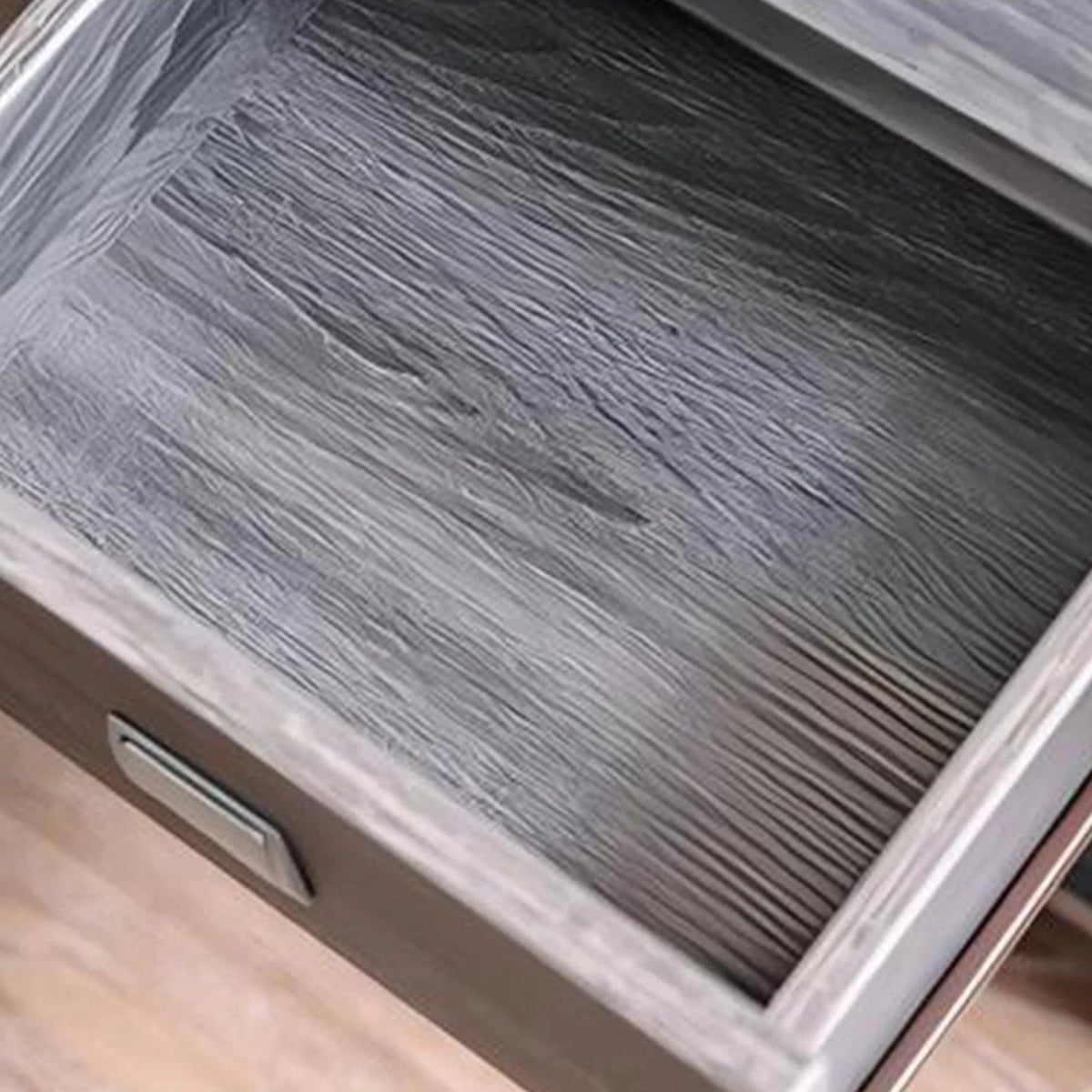 Gray end table drawer interior with metal bar pull and wood grain texture.