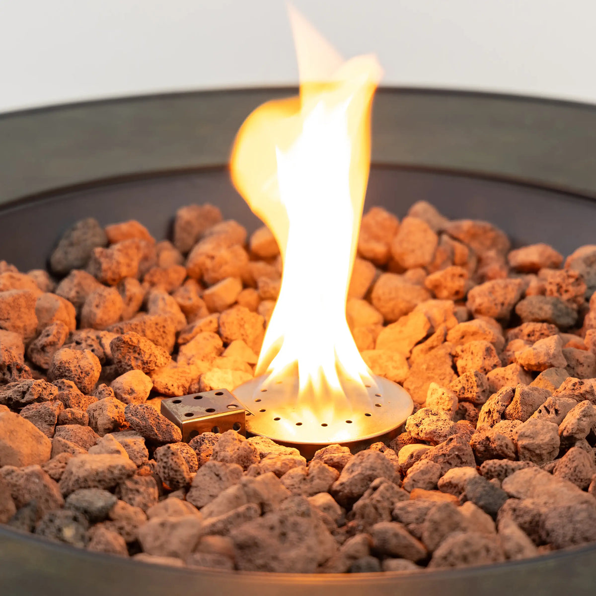 Flame burning over lava rocks inside a black circular gas fire pit
