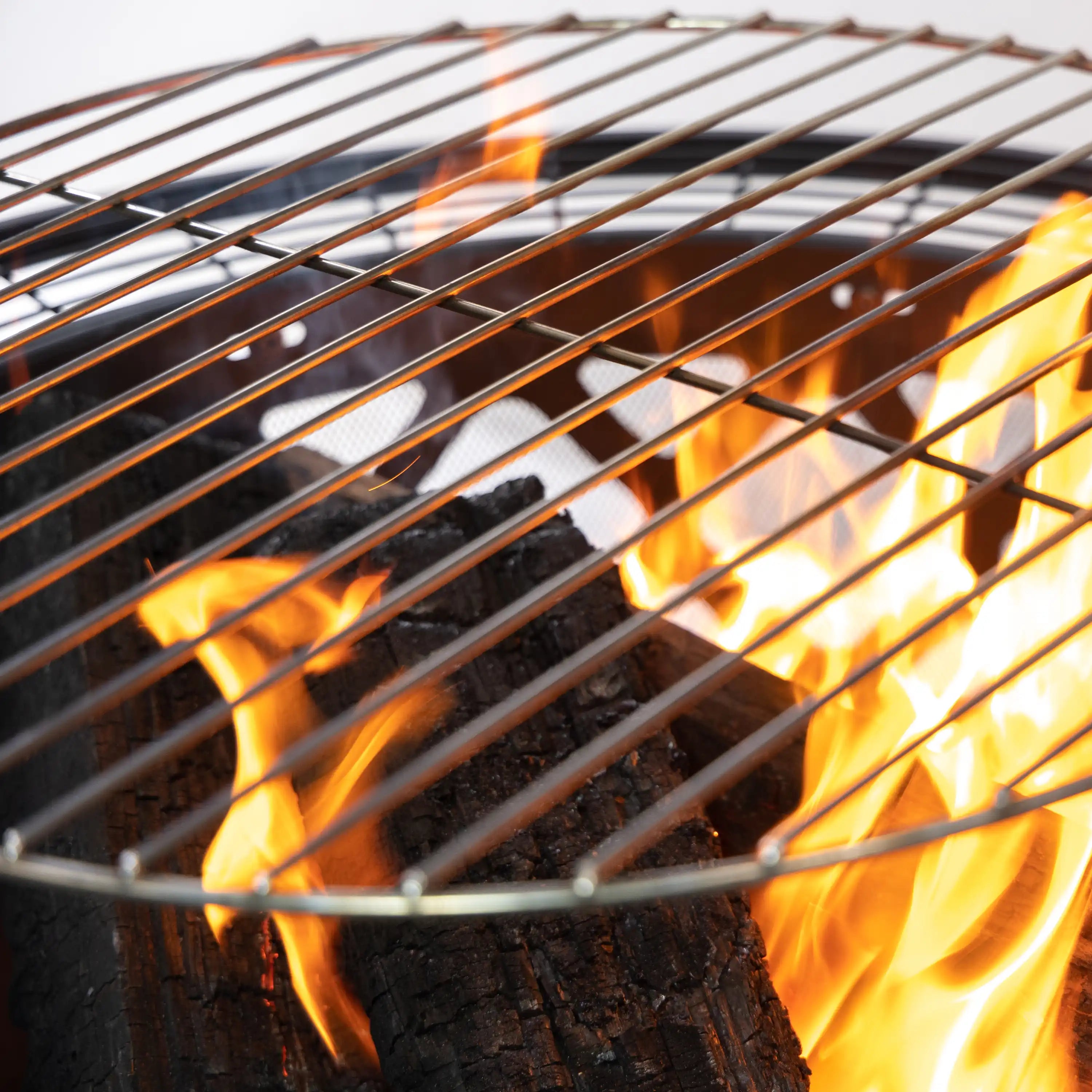 Close-up of burning firewood inside a steel fire pit on a wire grill grate