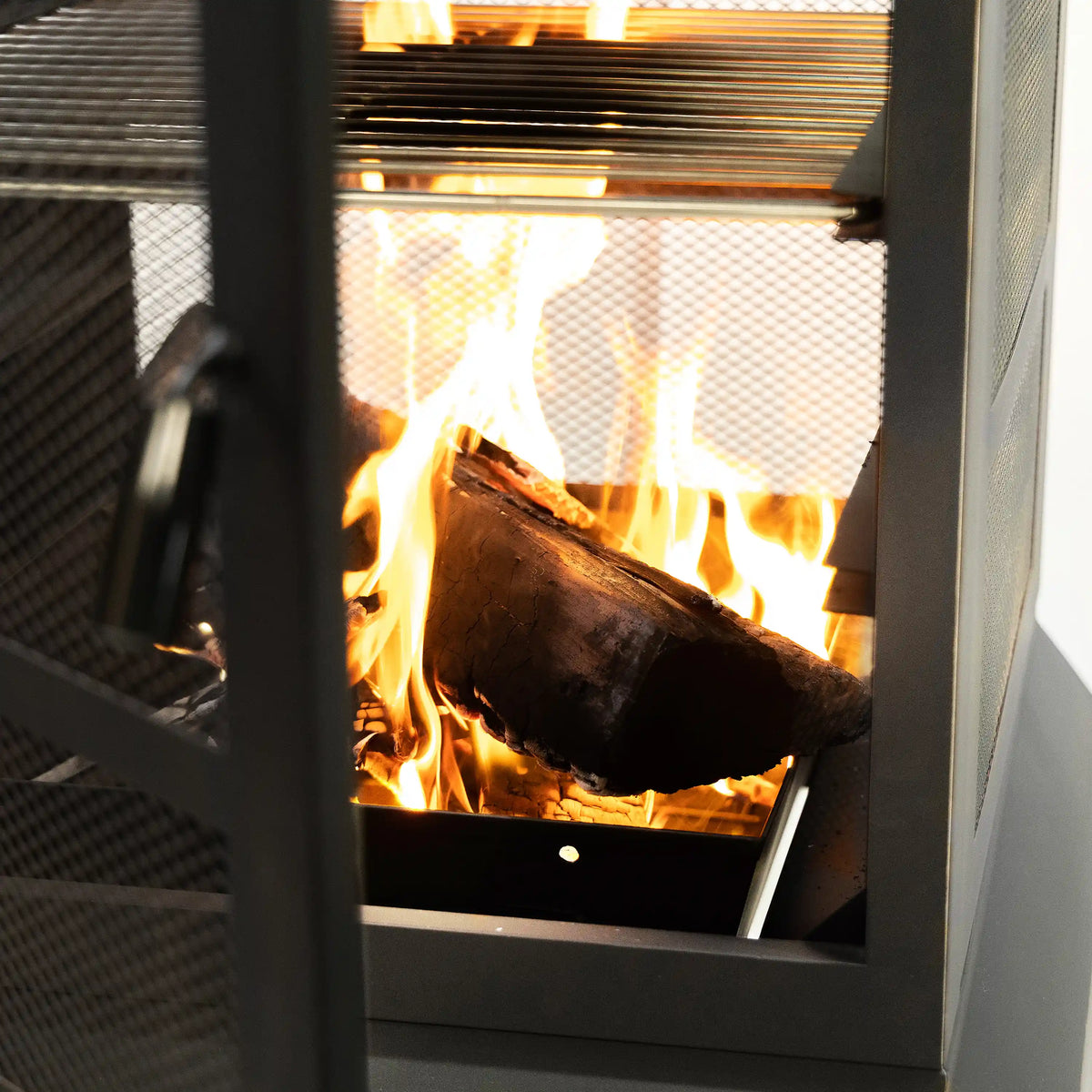 Burning wood inside mesh firebox of an outdoor steel woodburning fireplace