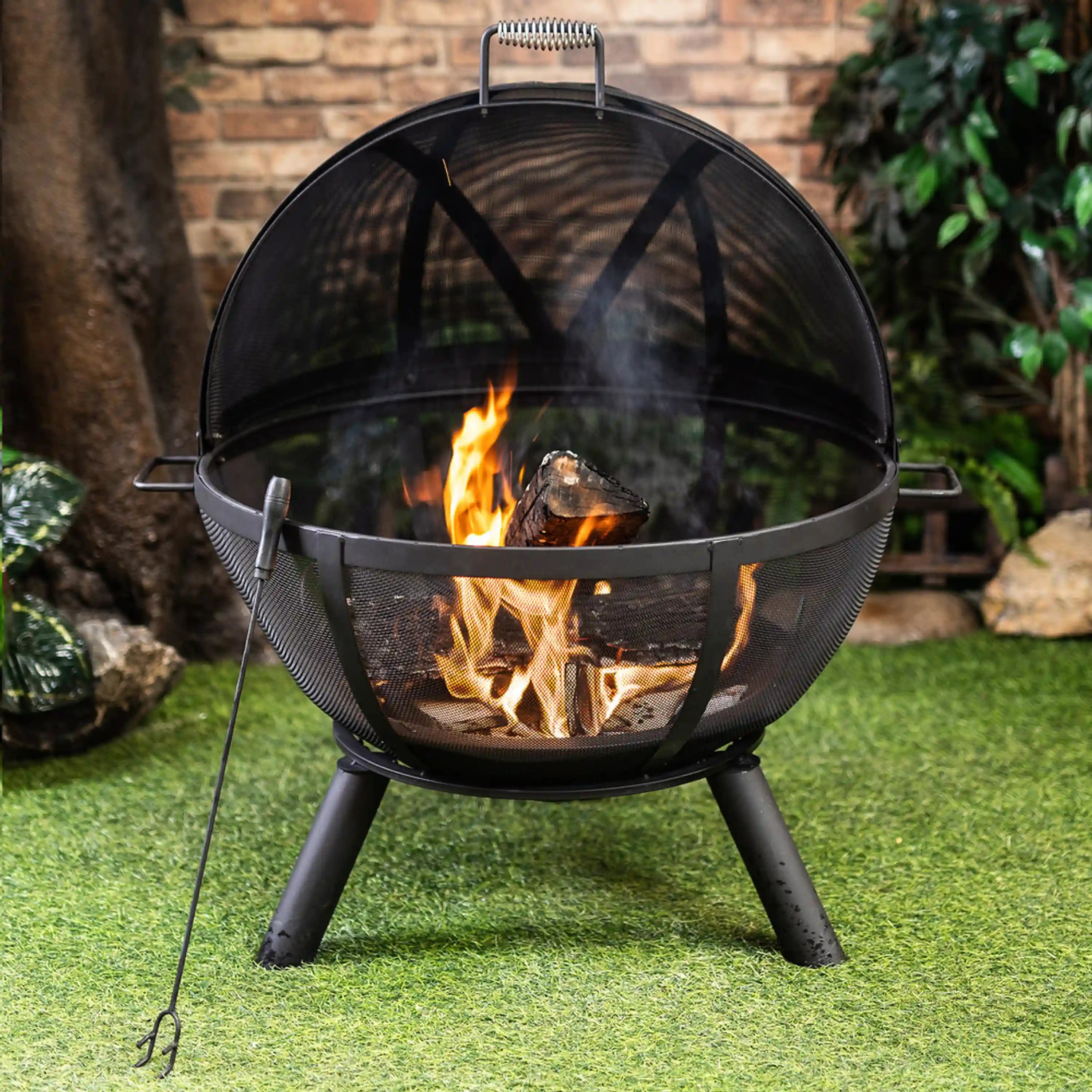 Outdoor sphere fire pit with black mesh dome, burning logs inside, three-leg base