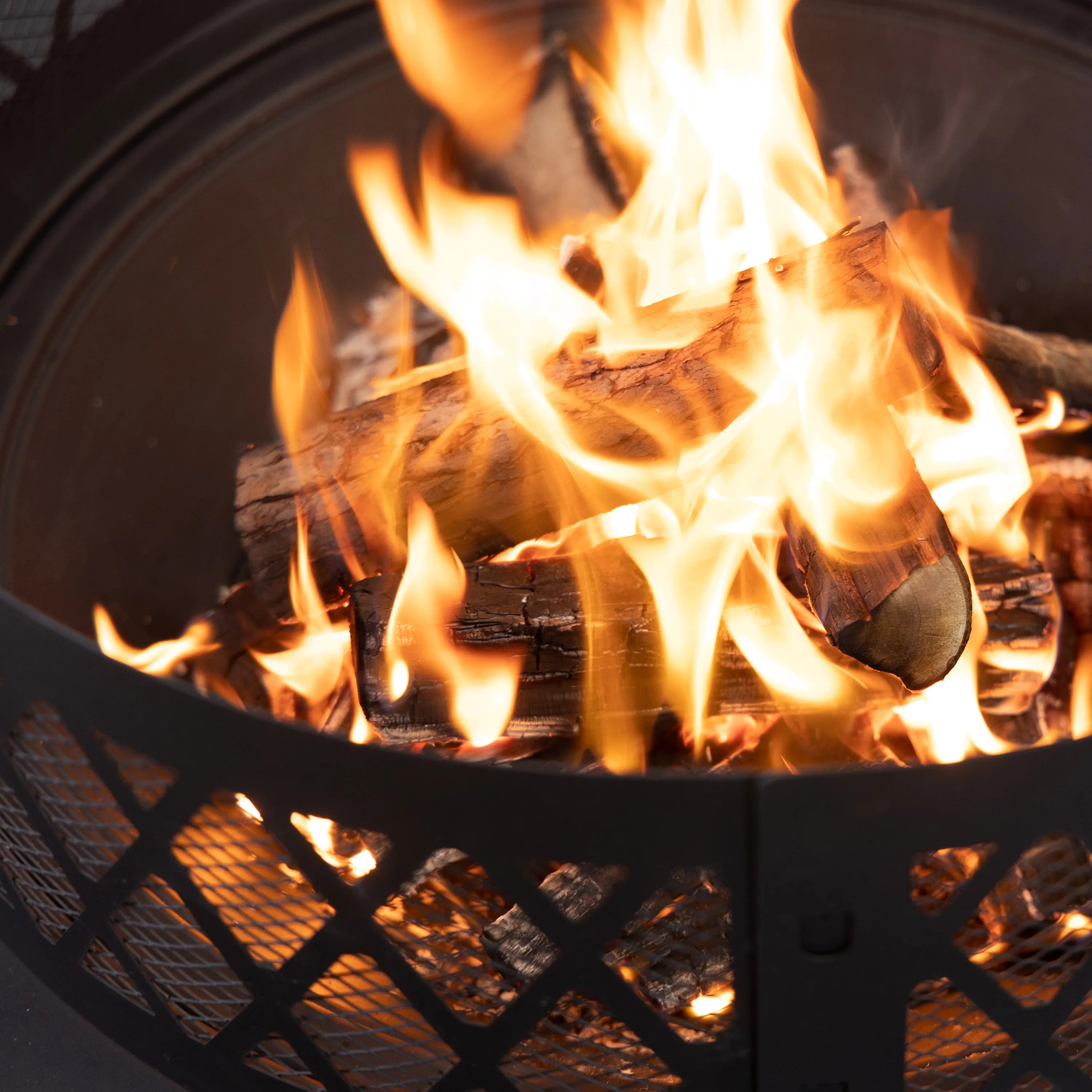 Wood-burning fire pit with flames inside black mesh lattice fire bowl.