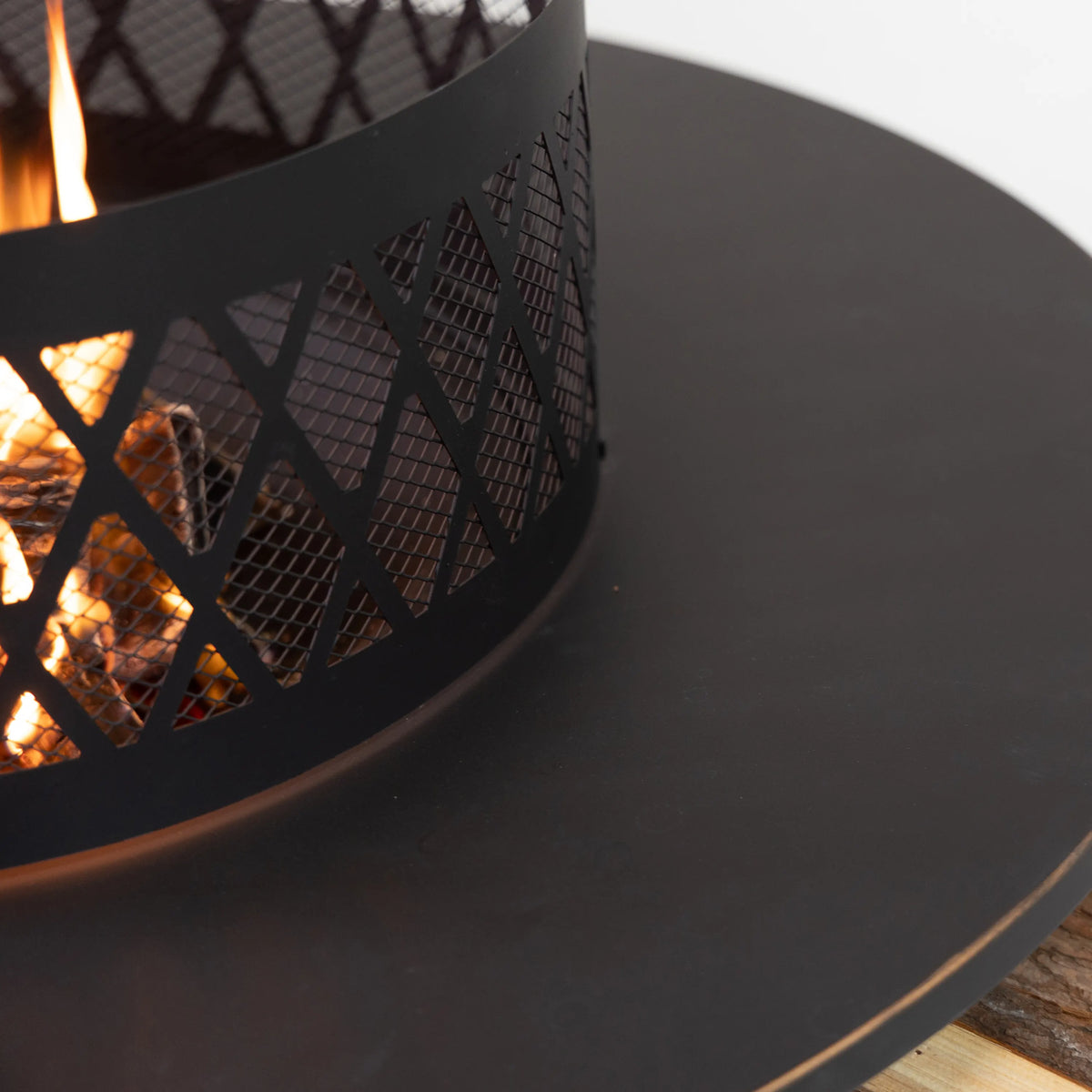 Outdoor steel fire pit, black mesh sides with open flame through lattice.