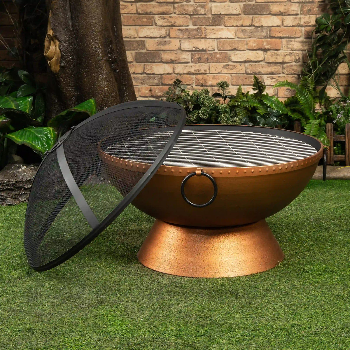 Round firepit on a pedestal base with mesh cover tilted beside it